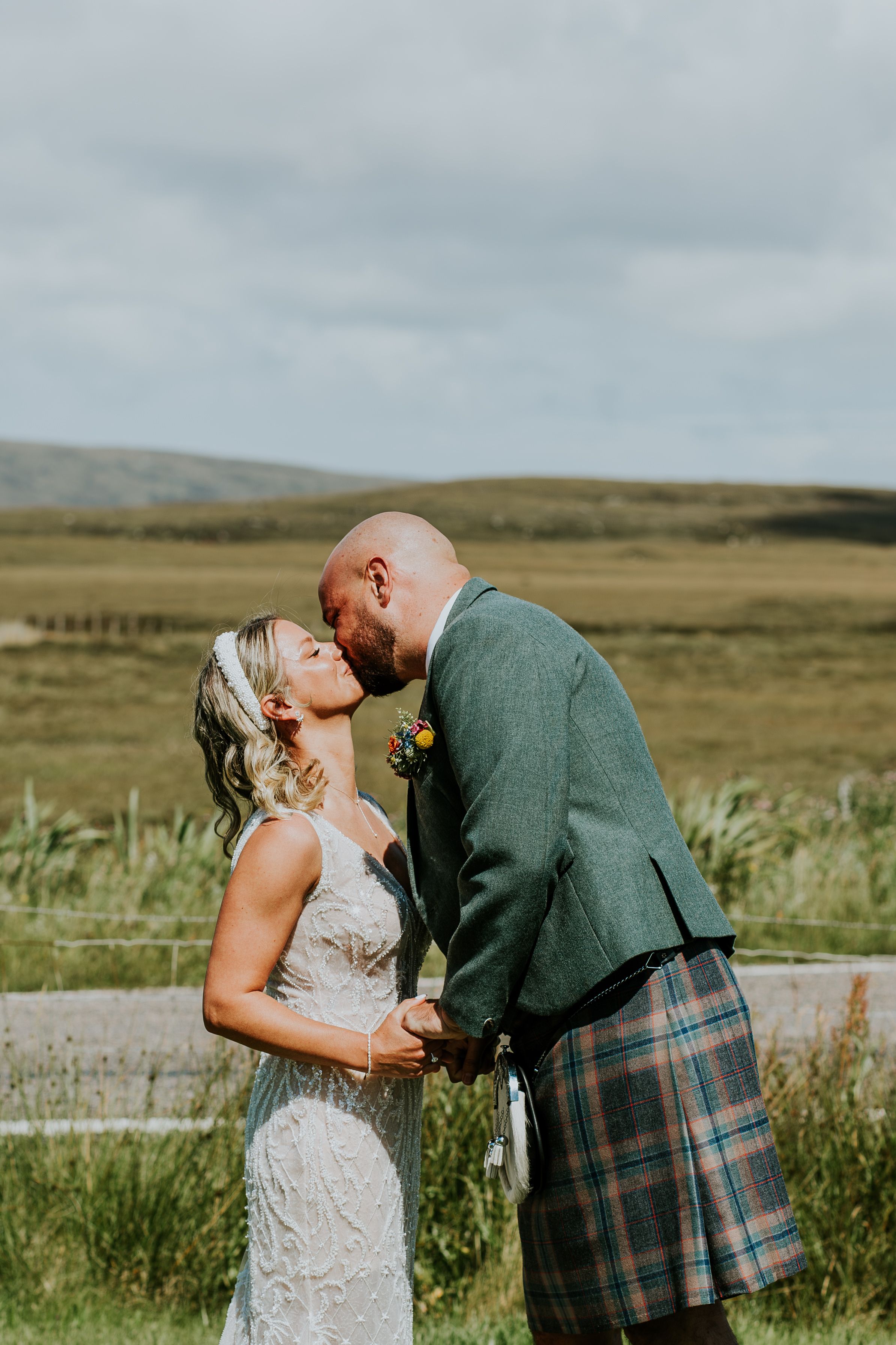 A couple shares an intimate moment in the Scottish countryside with rolling hills in the background.