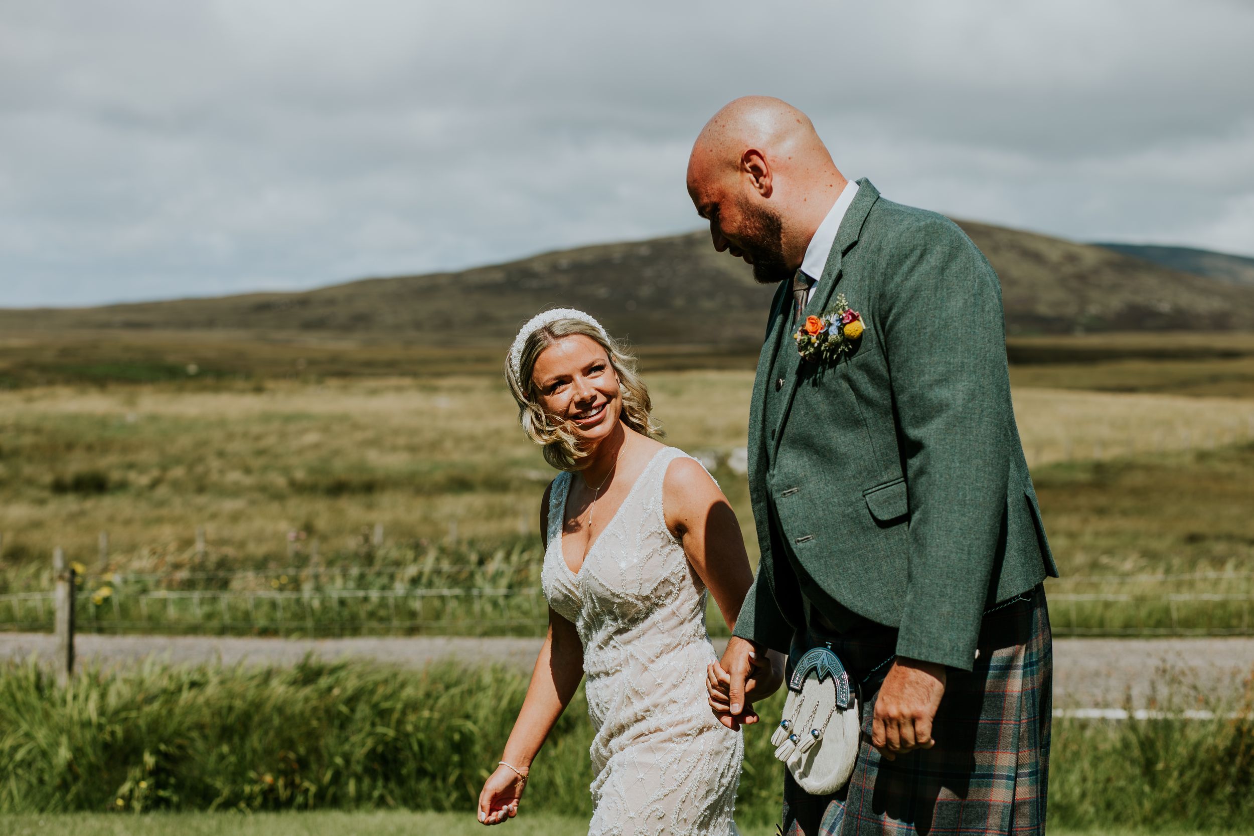 Couple in wedding attire share a joyful moment together on a scenic Scottish highland landscape.