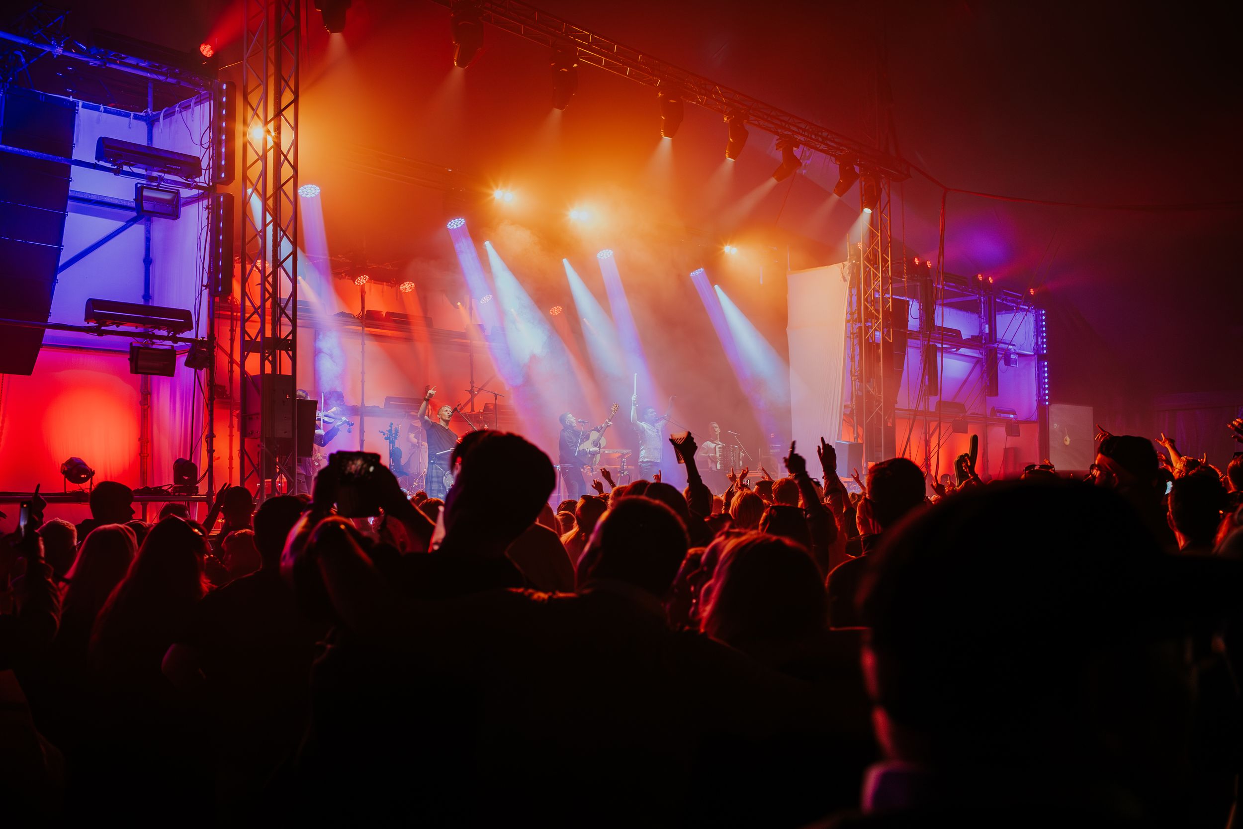 Concert crowd silhouettes with raised hands against red stage lighting and fog at a live music performance.