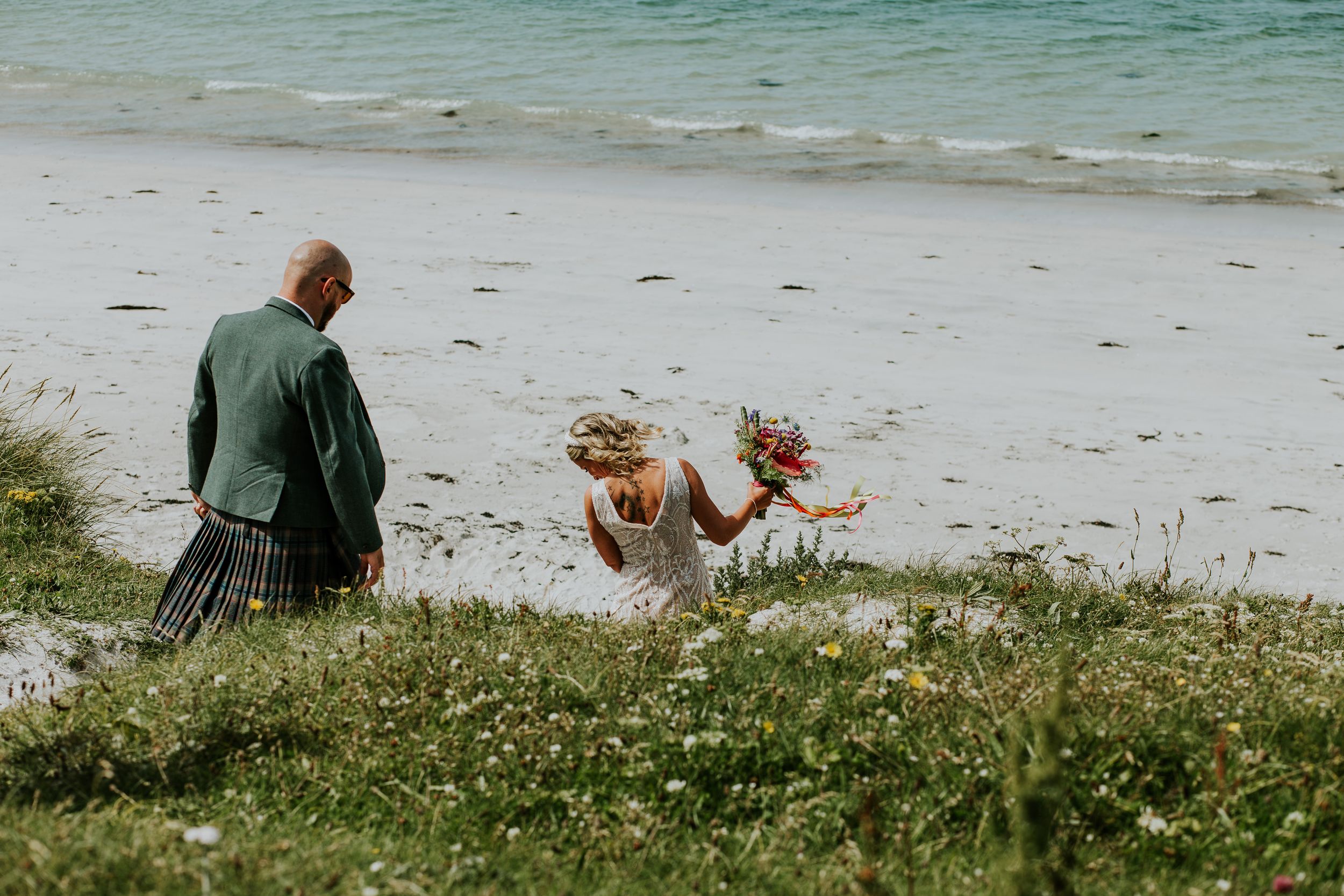 Group of friends enjoying a sunny day at a beach with grass and wildflowers in the foreground.