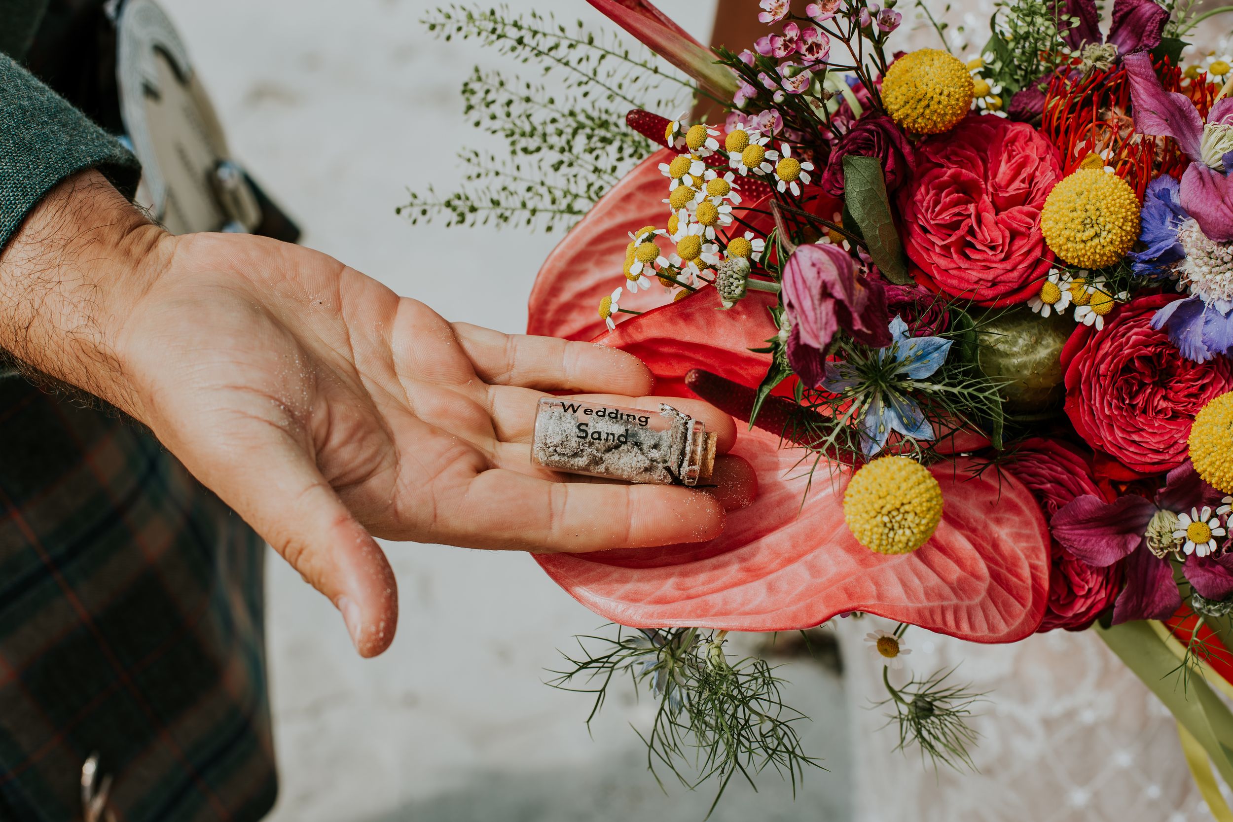 Close-up of hands showing wedding ring next to bright red and yellow floral bouquet with wildflowers and berries.
