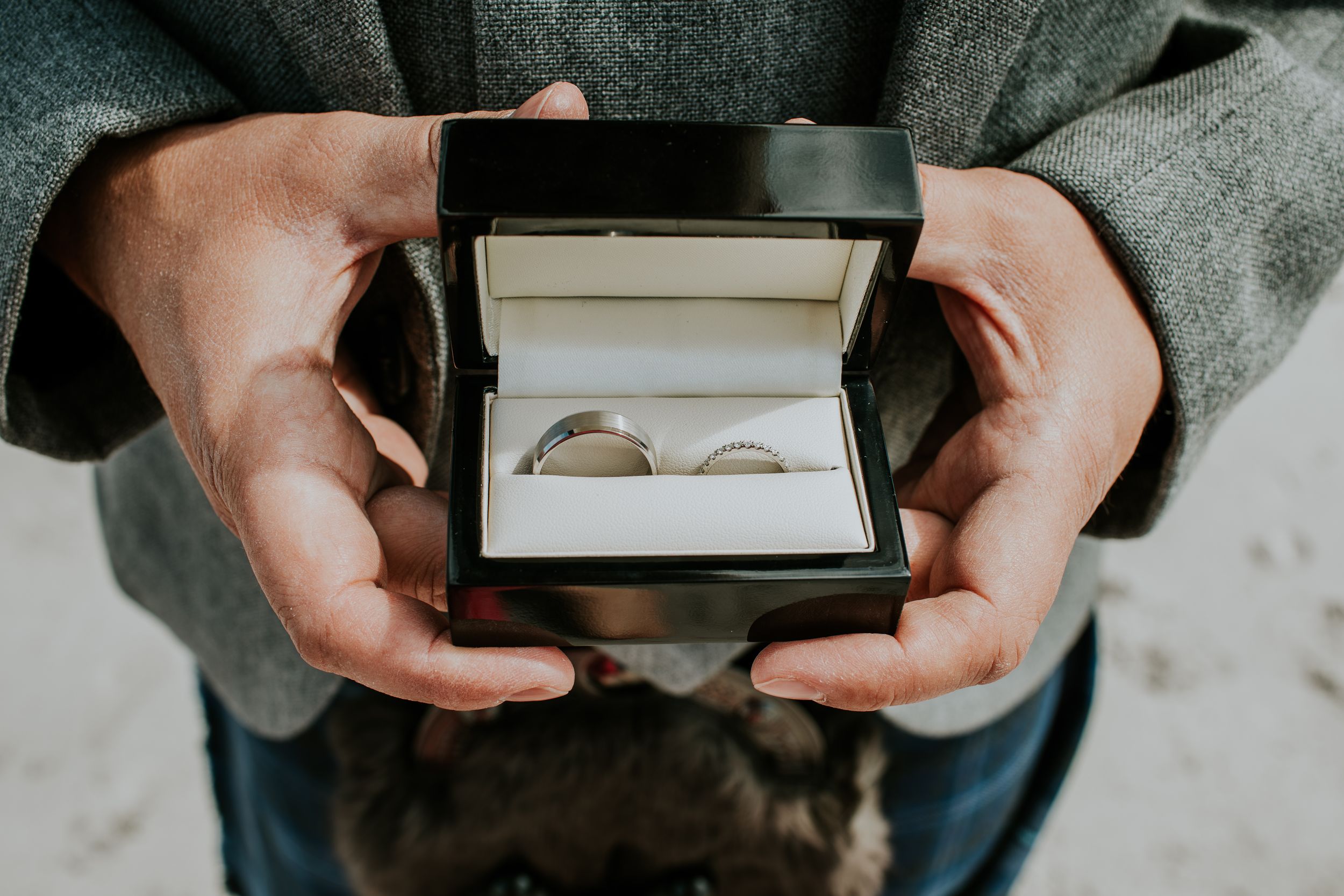 Hands holding a small black box with two wedding rings nestled inside.