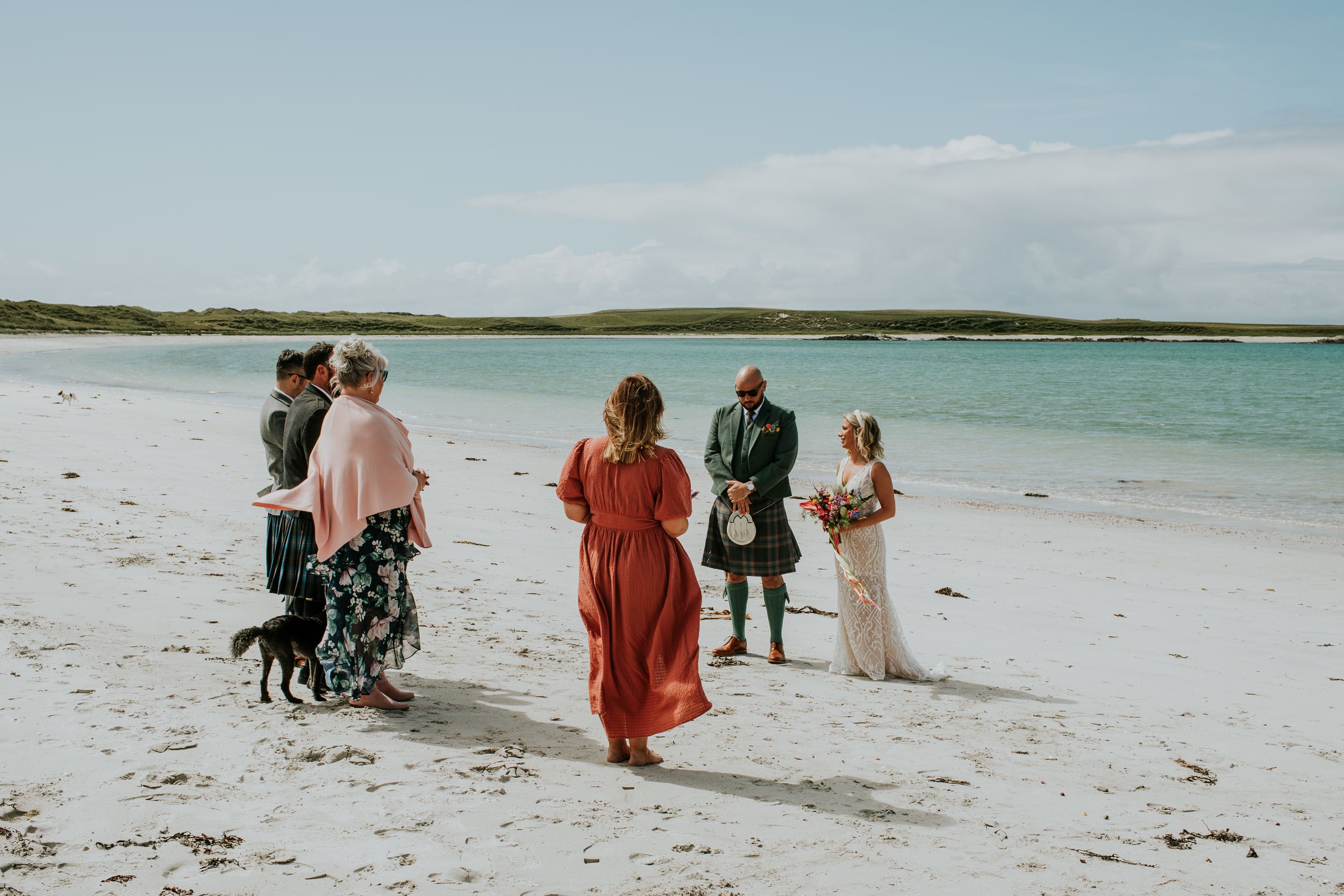 Small group of people and a dog walking together on a pristine white sandy beach with turquoise water.