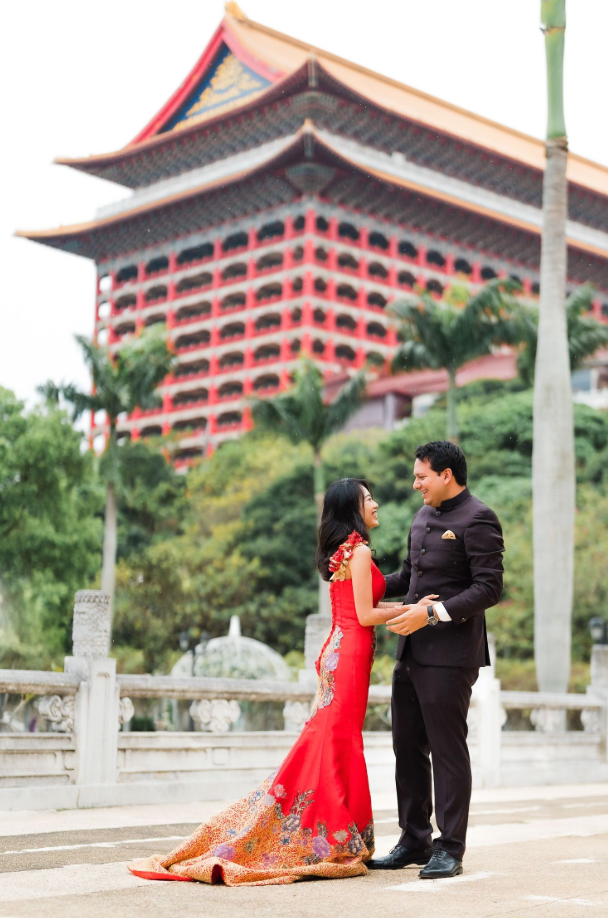 A couple in formal attire poses in front of the Grand Hotel in Taipei, with its iconic Chinese architecture visible.