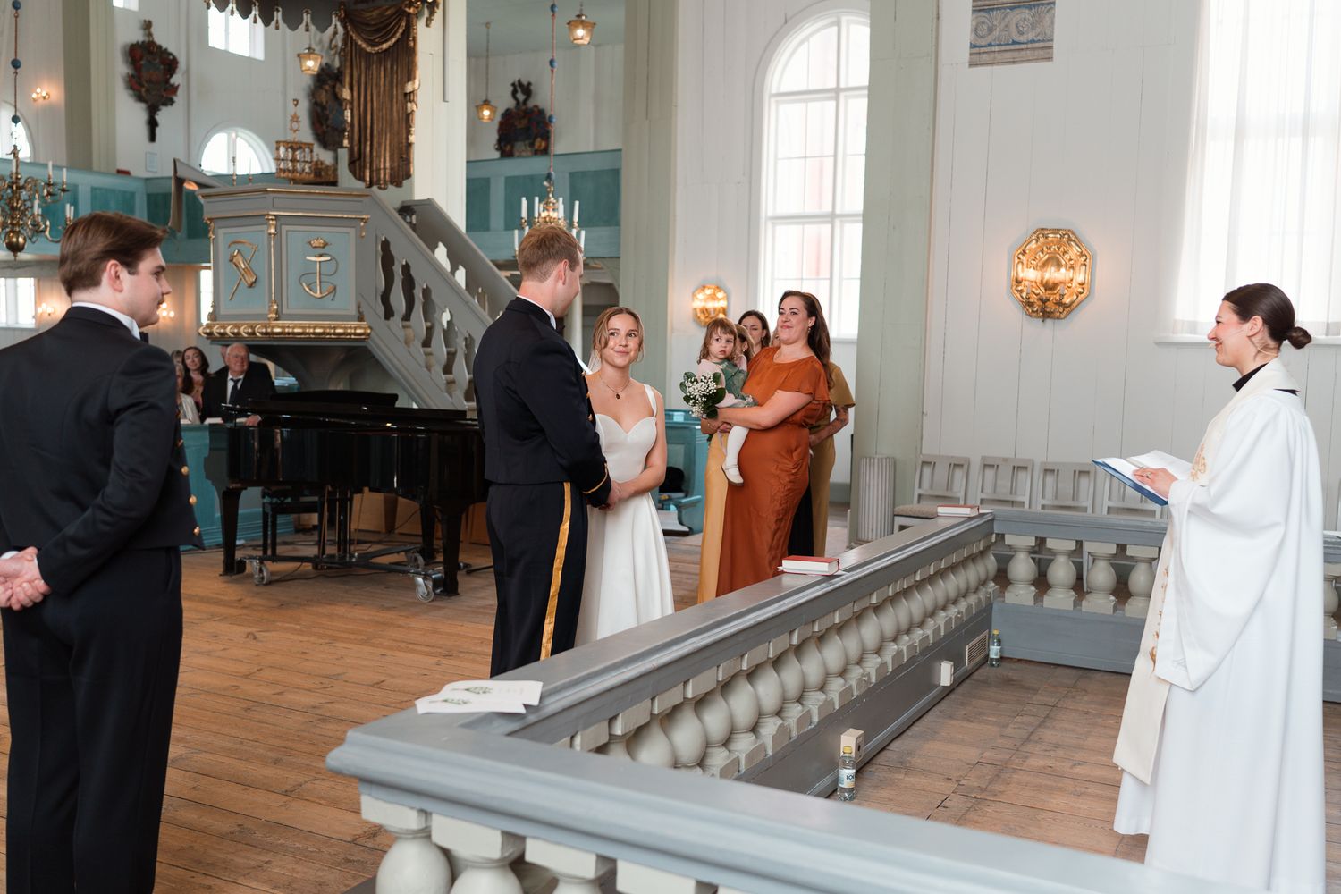 A group gathers for an indoor ceremony in a historic chapel with teal blue accents and elegant architectural details.