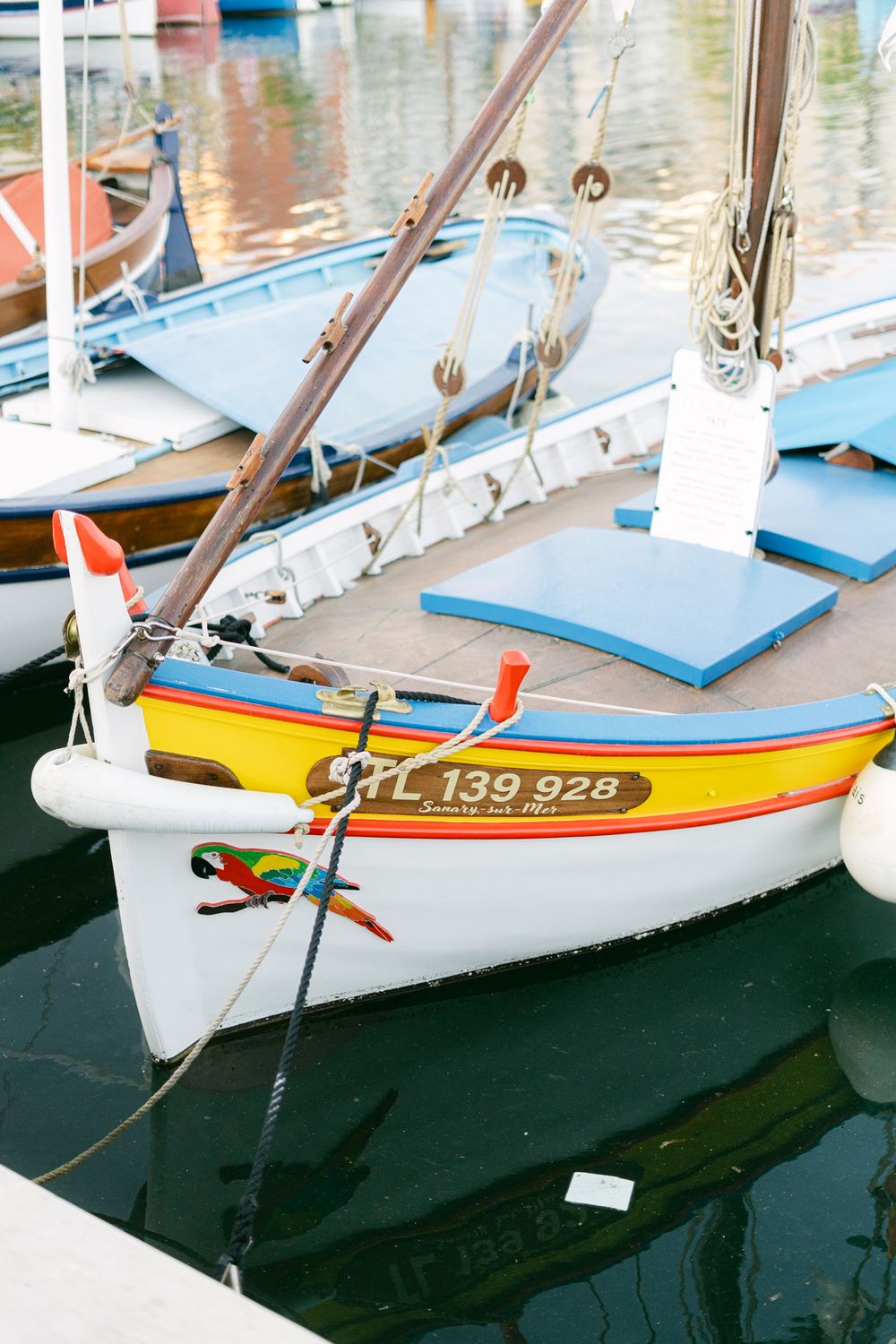 A colorful wooden sailboat with yellow and white hull moored in a marina alongside other small boats.