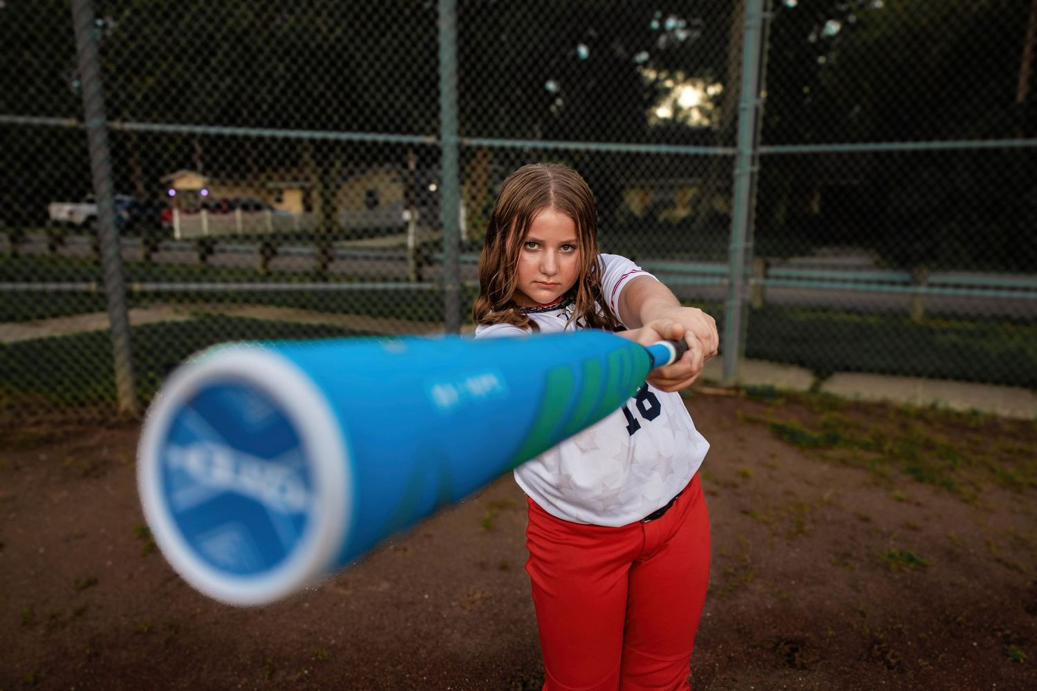 Softball player aims blue bat while wearing Bombers uniform on baseball field.