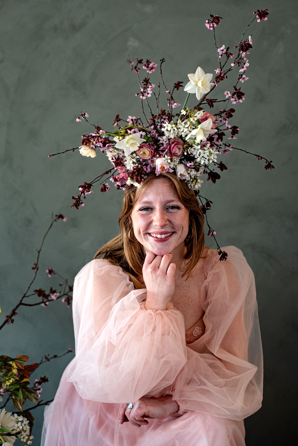 A romantic spring portrait with cherry blossoms and floral crown against a dark green backdrop in soft pink tulle dress.