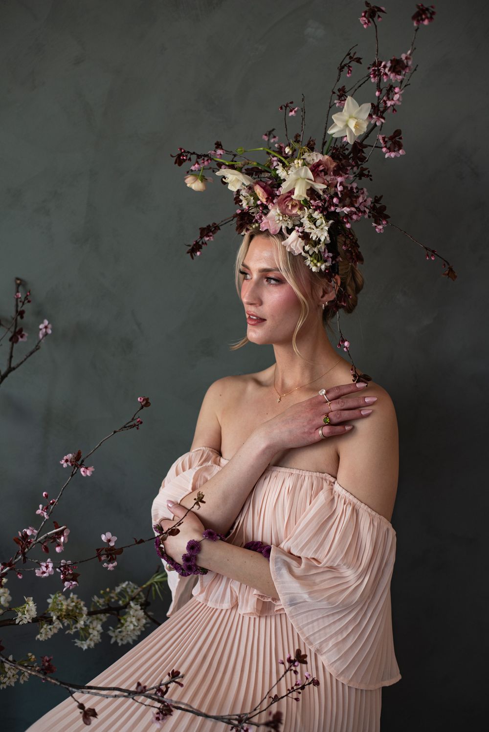 Ethereal portrait with cherry blossoms and pale pink pleated dress against moody gray background.