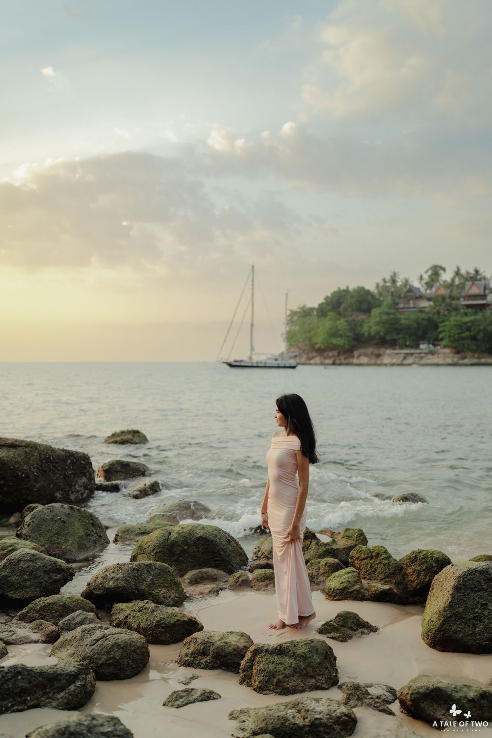 A scenic beach landscape with rocky outcrops and boats anchored in the distance at sunset.