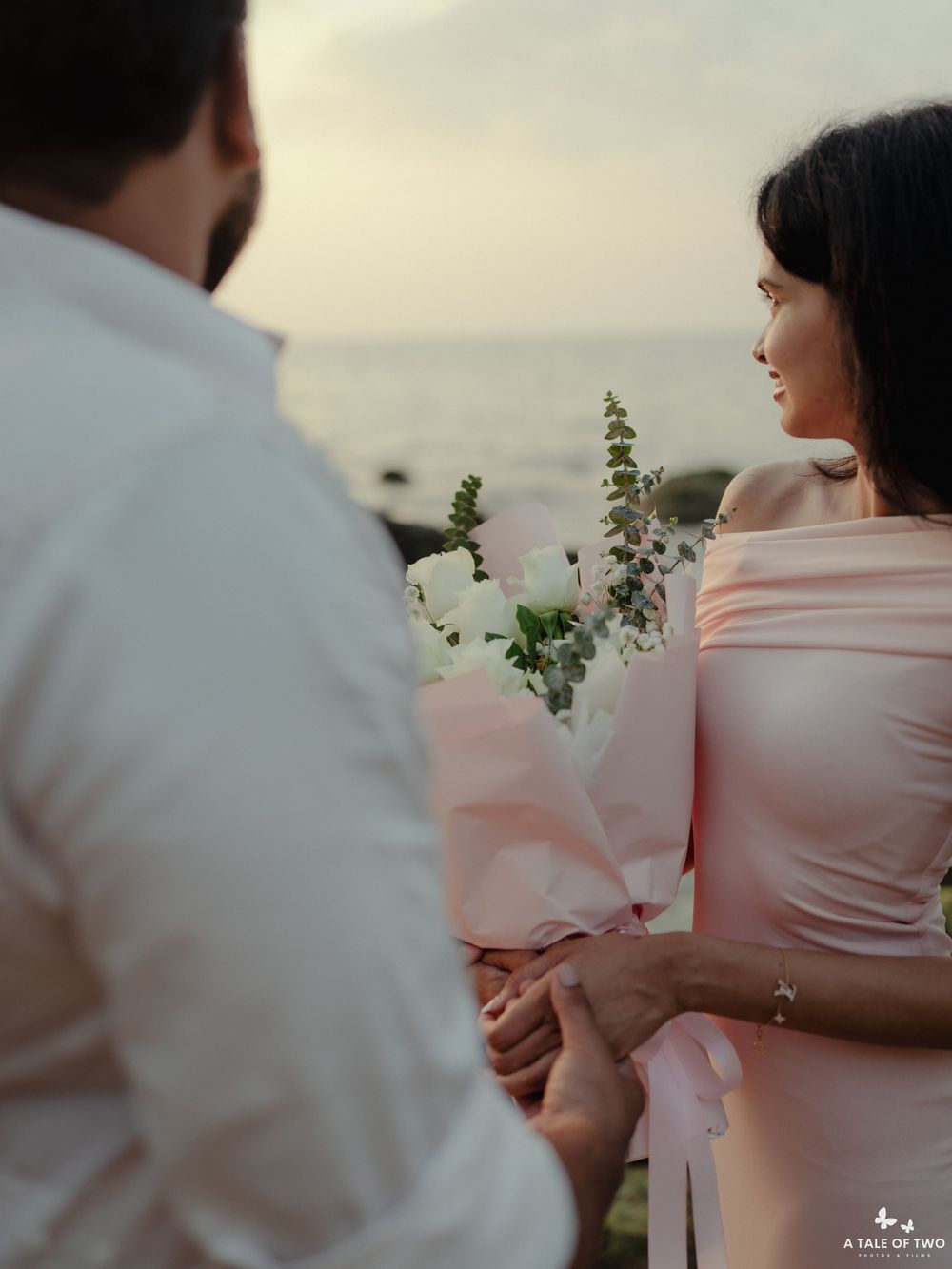 Intimate moment captured between couple with flowers during beach sunset.