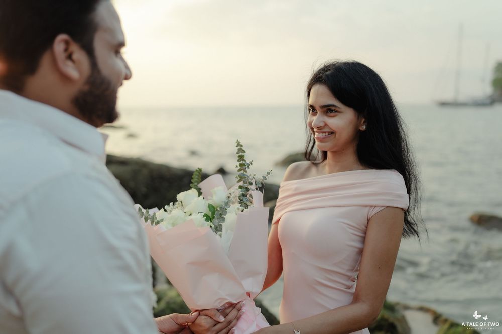 Couple sitting on beach at sunset sharing romantic moments with white flowers and blush pink dress details.