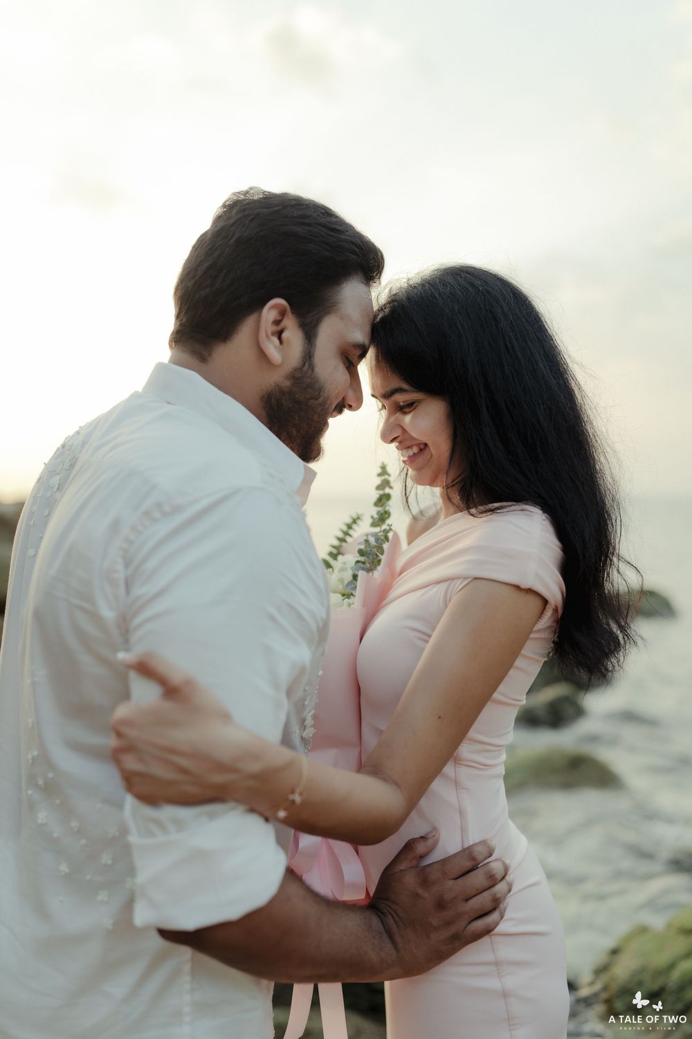 A romantic moment captured between two people in light colored clothing on a beach at sunset.