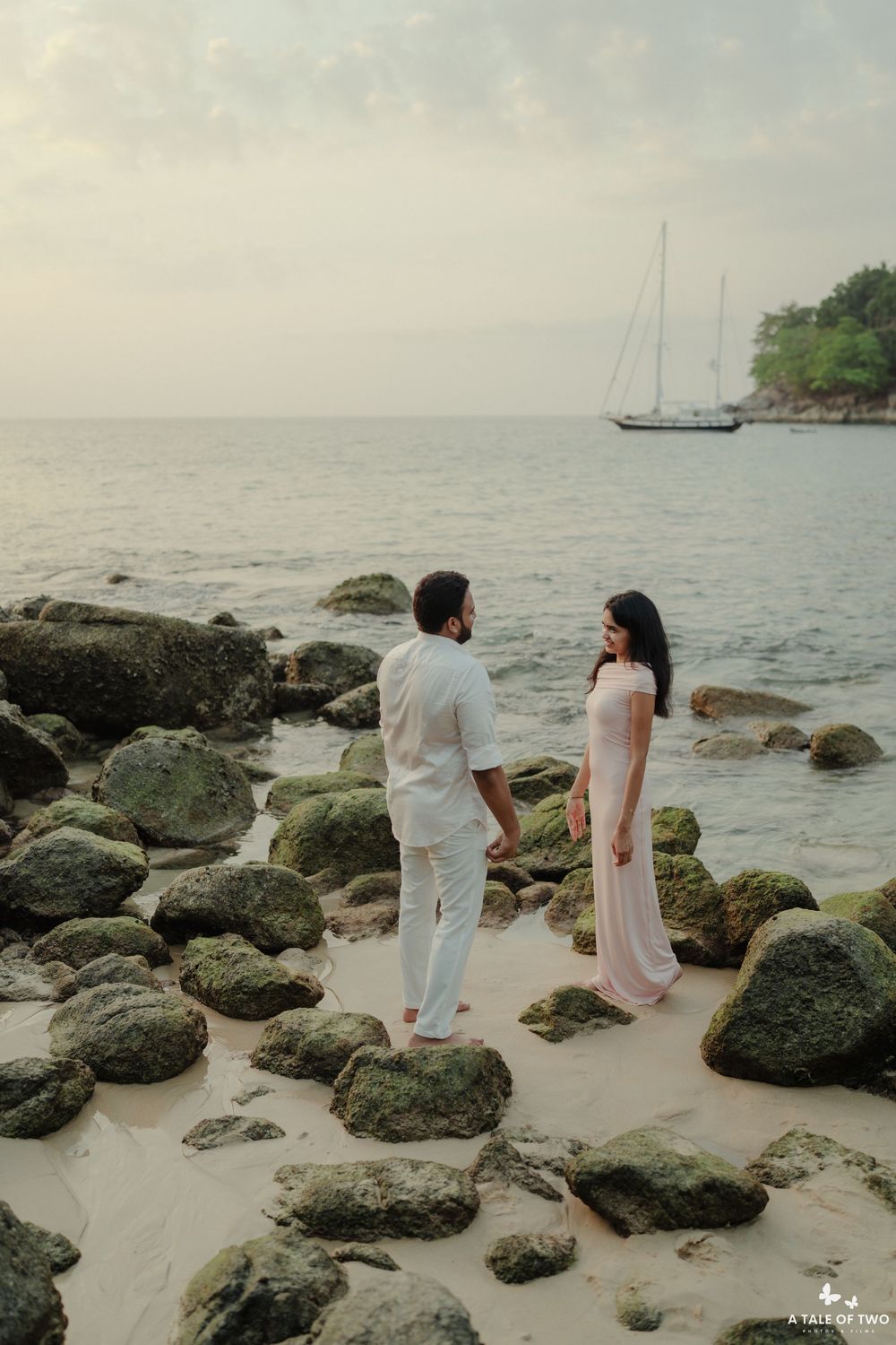 Two people in coordinated outfits stand among rocky formations on a beach at dusk.