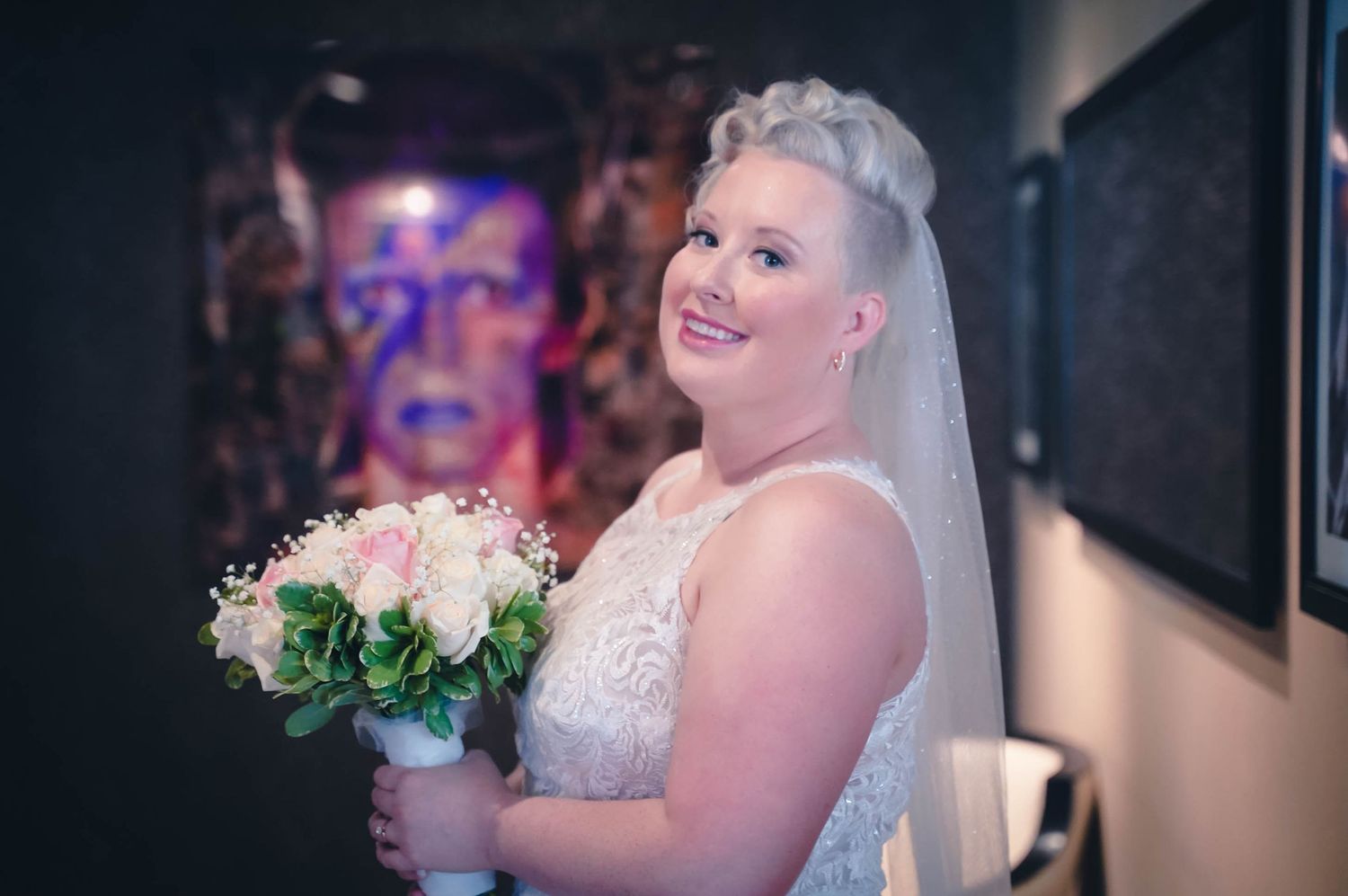 Bride holding her bouquet and posing in front of a David Bowie portrait at JAG Hotel, St. John's, Newfoundland.