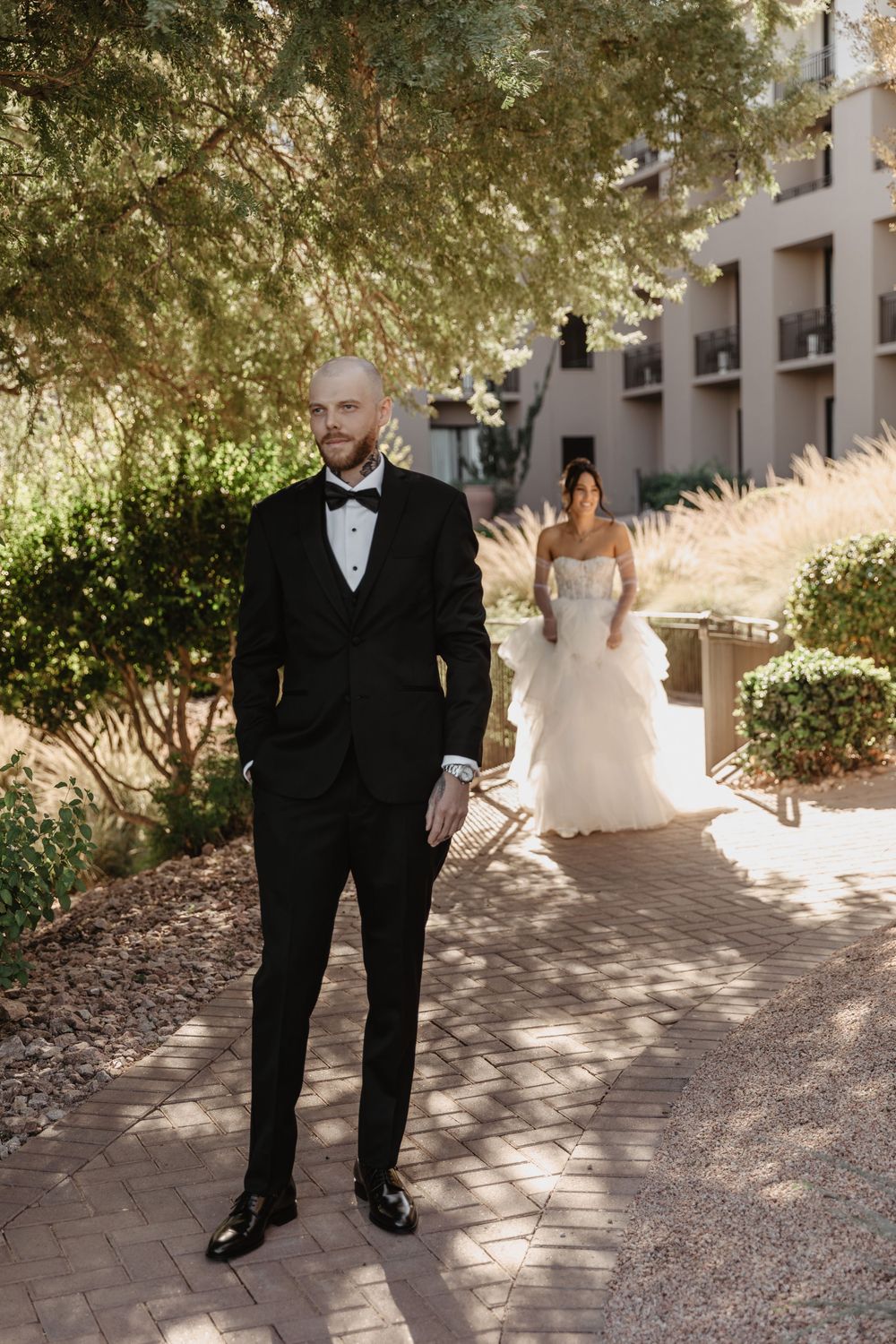 A couple shares a romantic first look moment in a sunlit garden walkway before their wedding ceremony.