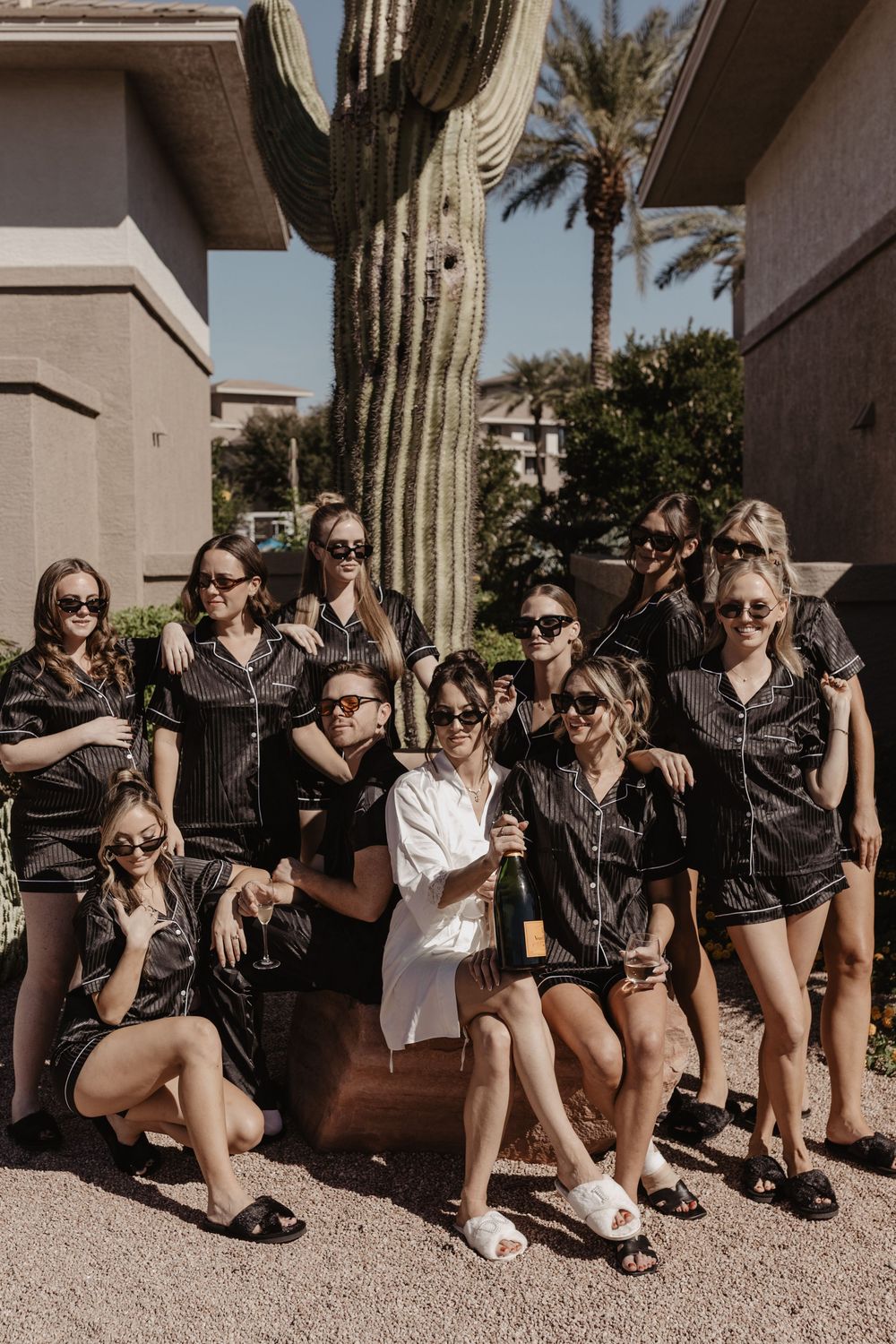 Group of friends in sunglasses and black outfits lounging together outdoors on a sunny day.