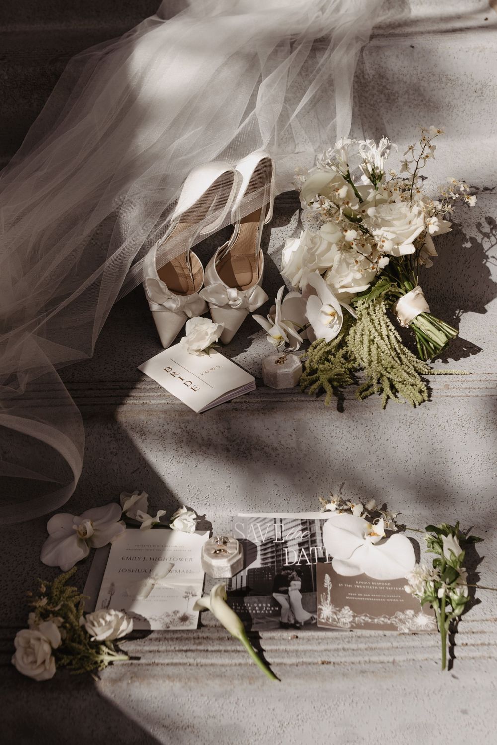 Wedding details including white bridal shoes, delicate veil, floral bouquet, and vintage photographs arranged on light surface.