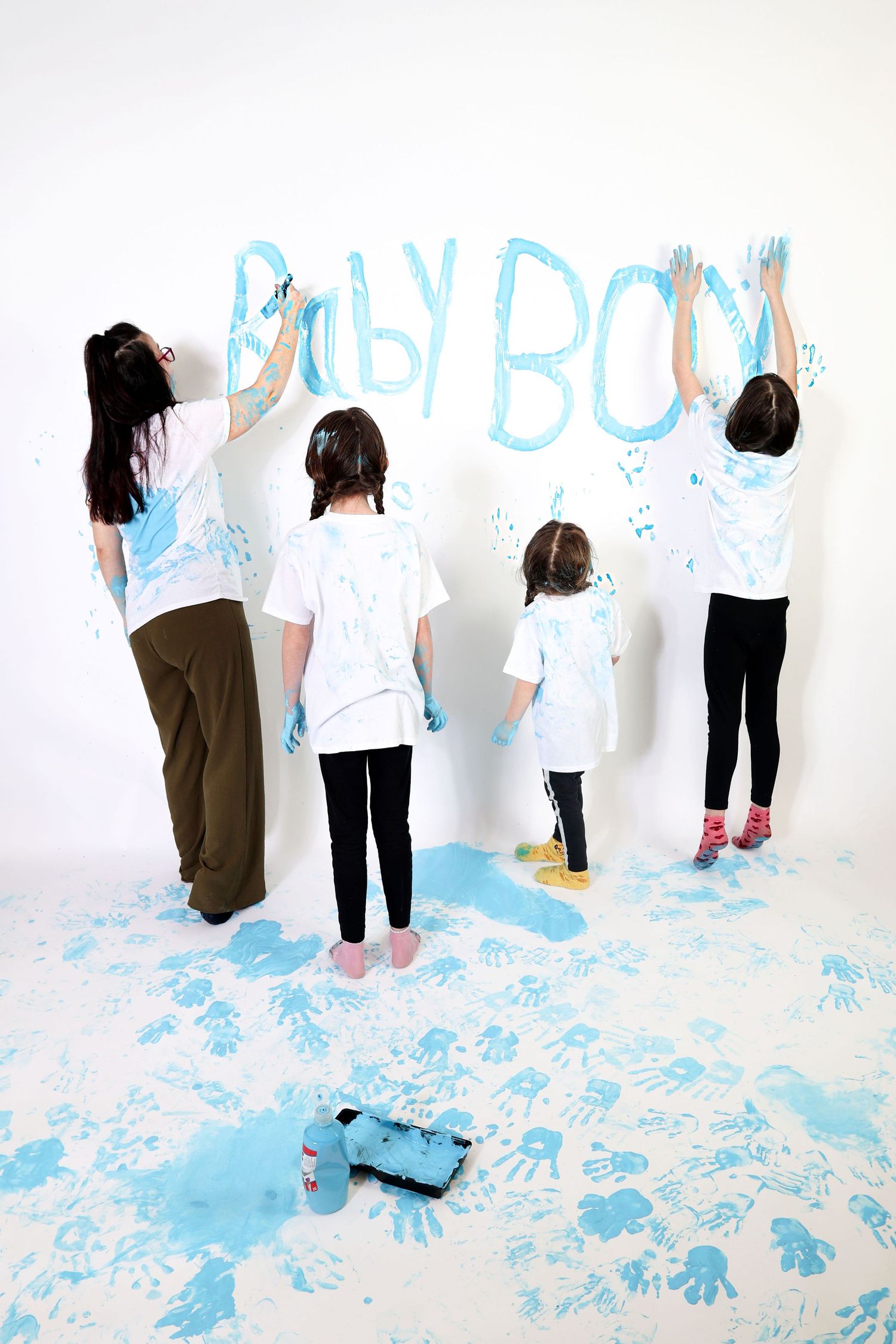 People in white shirts and dark pants create collaborative artwork by painting on a large white wall with blue paint.