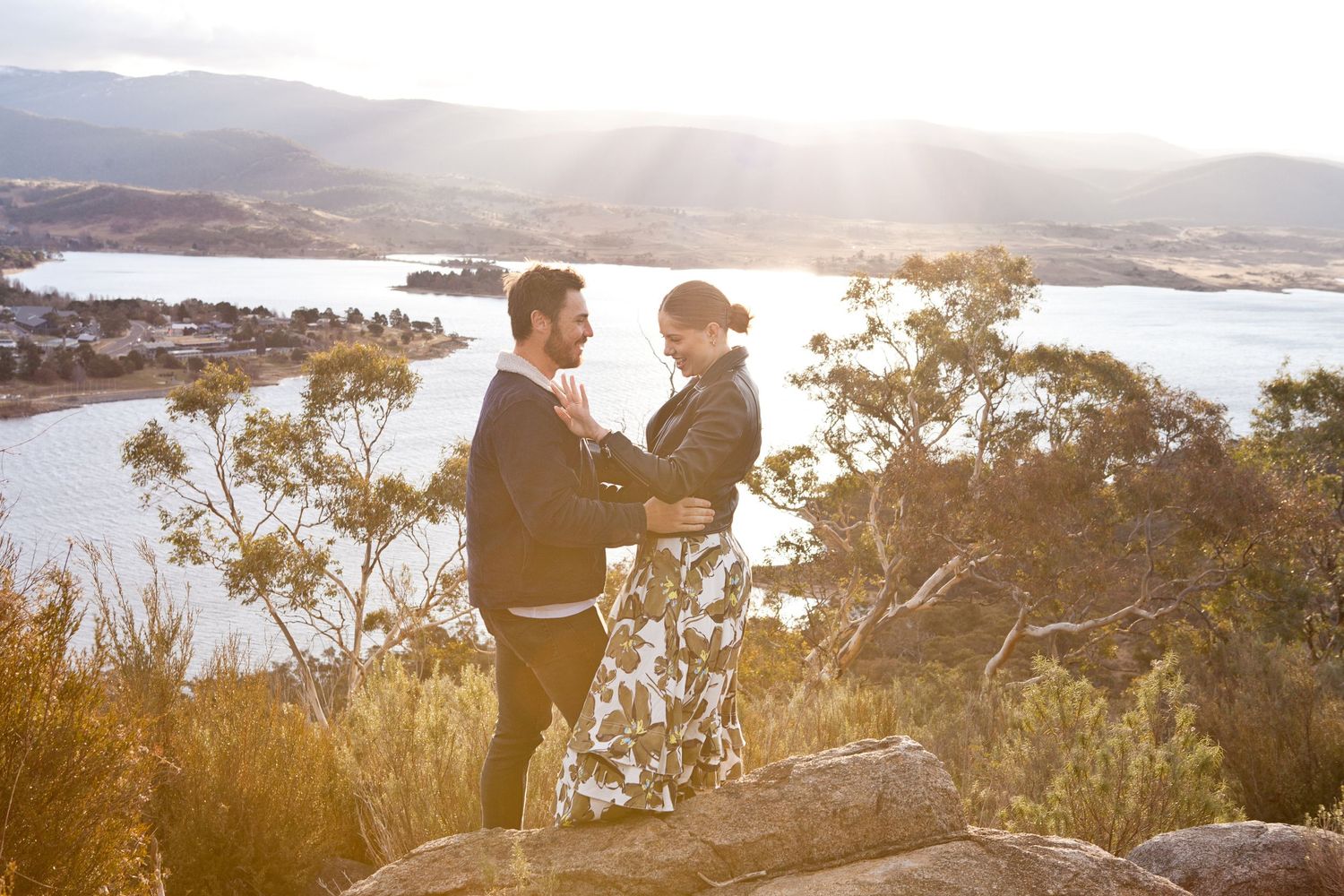 A couple shares a special moment during a proposal in front of a scenic mountain and lake views