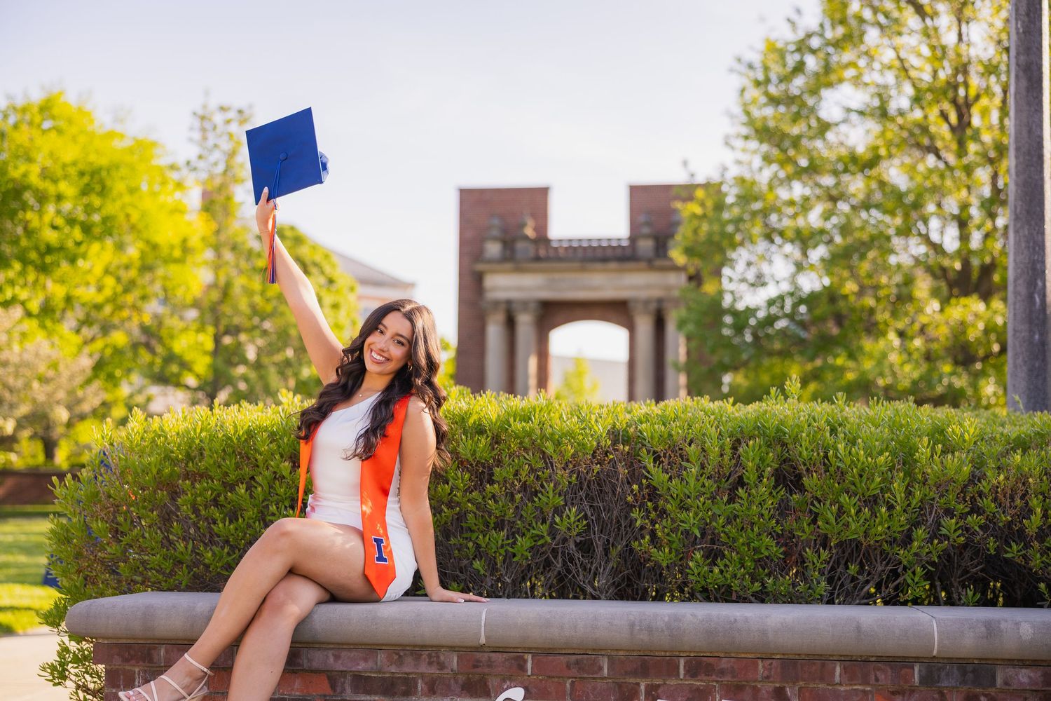 UIUC graduate holding her cap up in front of Hallene Gateway