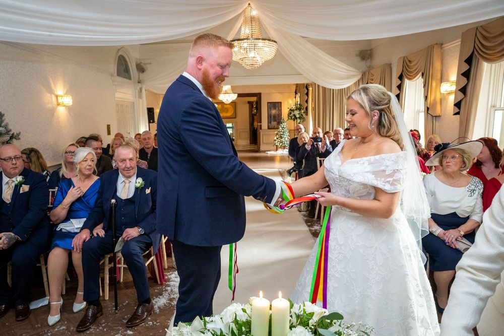 Bride and groom performing colorful handfasting ceremony at candlelit altar during wedding.
