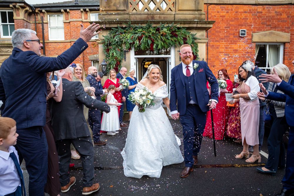 Newlywed couple walking through joyful confetti shower outside brick wedding venue after ceremony.