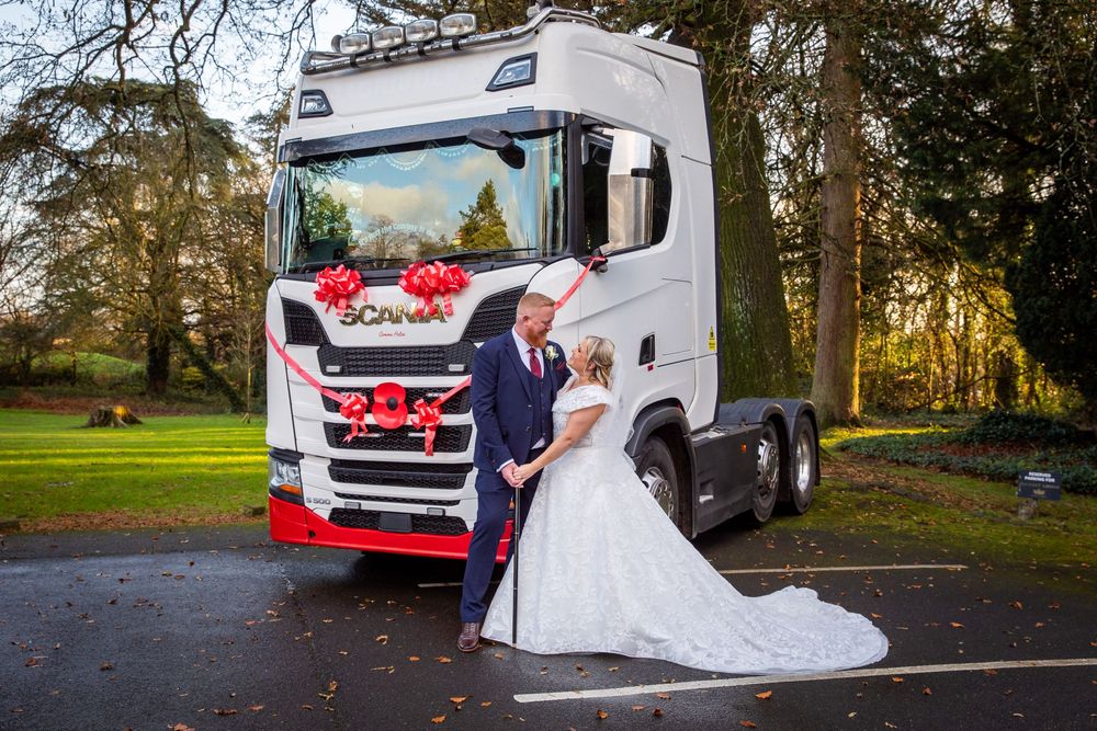 Bride and groom pose together in front of decorated white Scania truck at outdoor wedding.