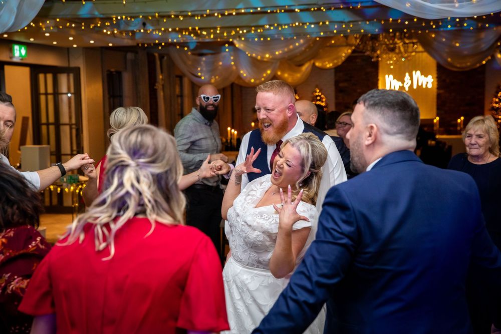 Bride and groom dance joyfully with guests at lively festive wedding reception celebration.