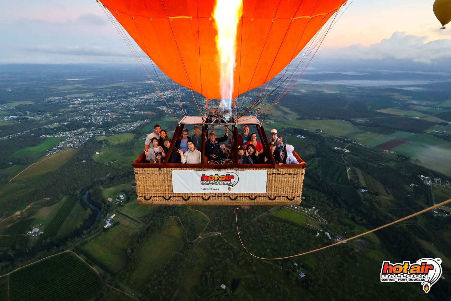 Hot air balloon ride with passengers soaring high above lush green countryside landscape at sunrise. Cairns Australia