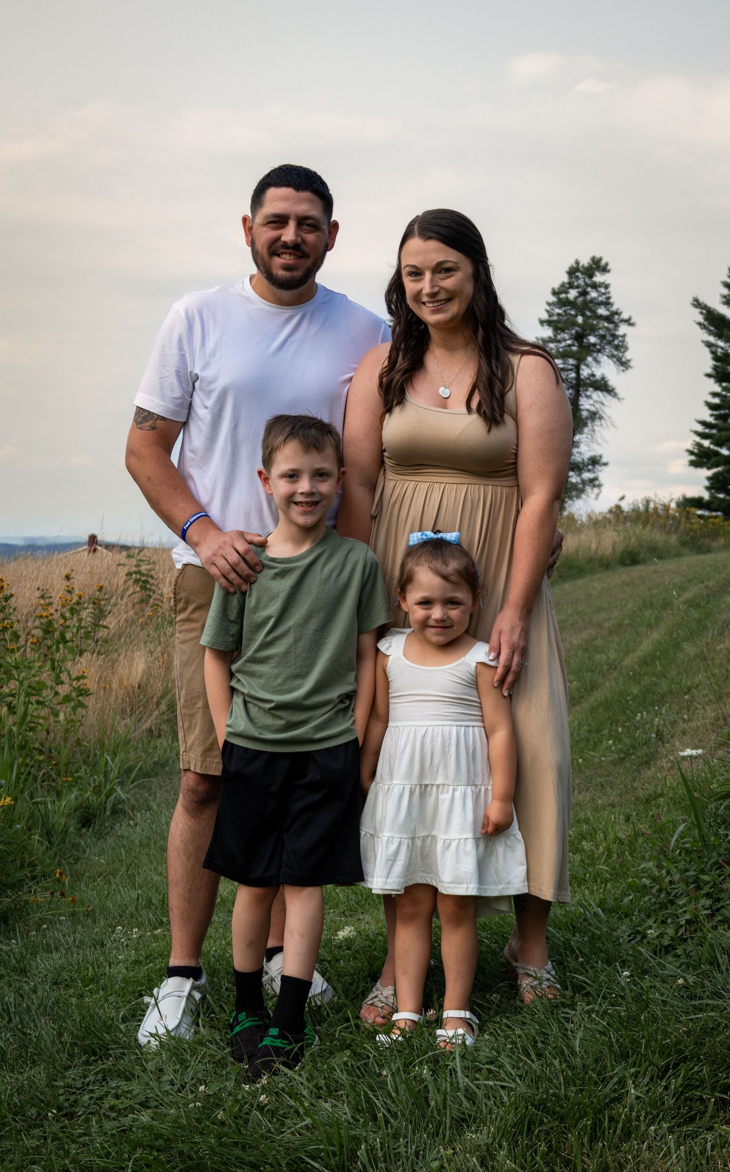 Pregnant woman in white dress poses with toddler and husband holding ultrasound photos in bright studio.