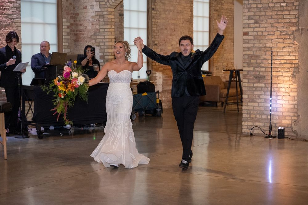 Couples dancing together during a wedding reception in an elegant brick-walled venue with crystal chandeliers.