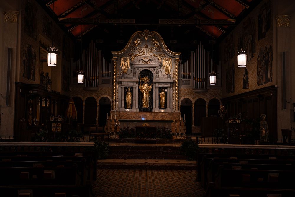 Interior view of a grand church sanctuary with ornate architecture, wooden beams, and religious artwork on display.