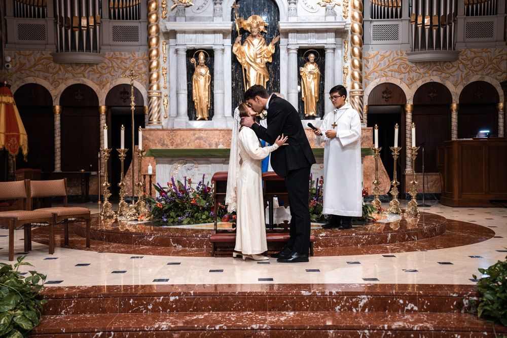 A wedding ceremony takes place inside an ornate church with gothic arches and decorative altar in the background.