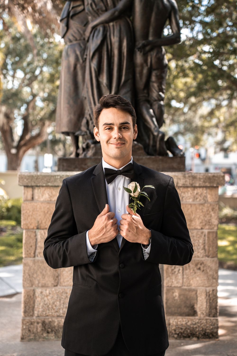 A person in a black suit poses in a series of shots against a stone wall backdrop in an outdoor setting.