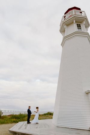 Couple exchange vows in front of lighthouse at the ocean in romantic coastal wedding on Price Edward Island, PEI wedding photos Canada