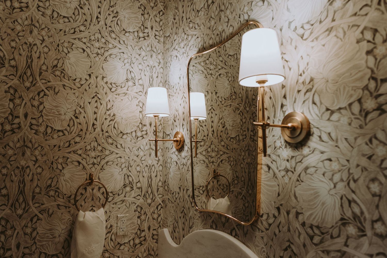 Elegant bathroom wall sconces illuminate an ornate wallpaper pattern in warm golden tones.