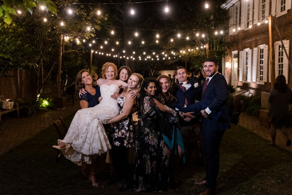 Wedding guests dance and celebrate under twinkling string lights at an outdoor evening reception.
