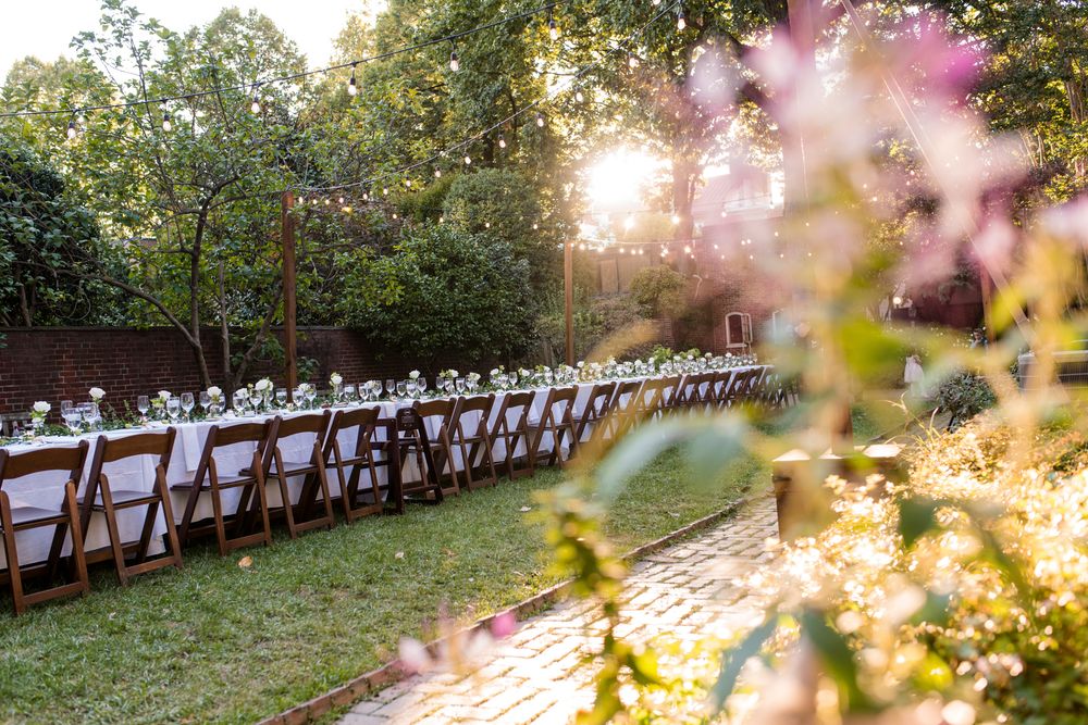 Long tables set for an elegant outdoor wedding reception under golden sunlight with pink cherry blossoms in the foreground.