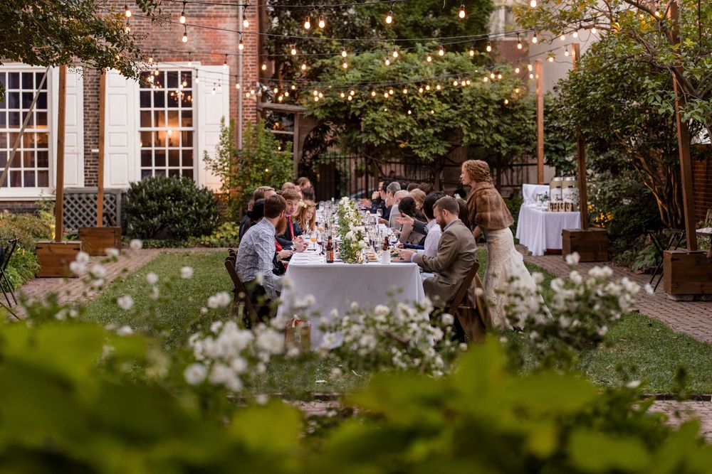 People enjoy an elegant outdoor garden party with string lights and tables set for dining in a lush courtyard setting.