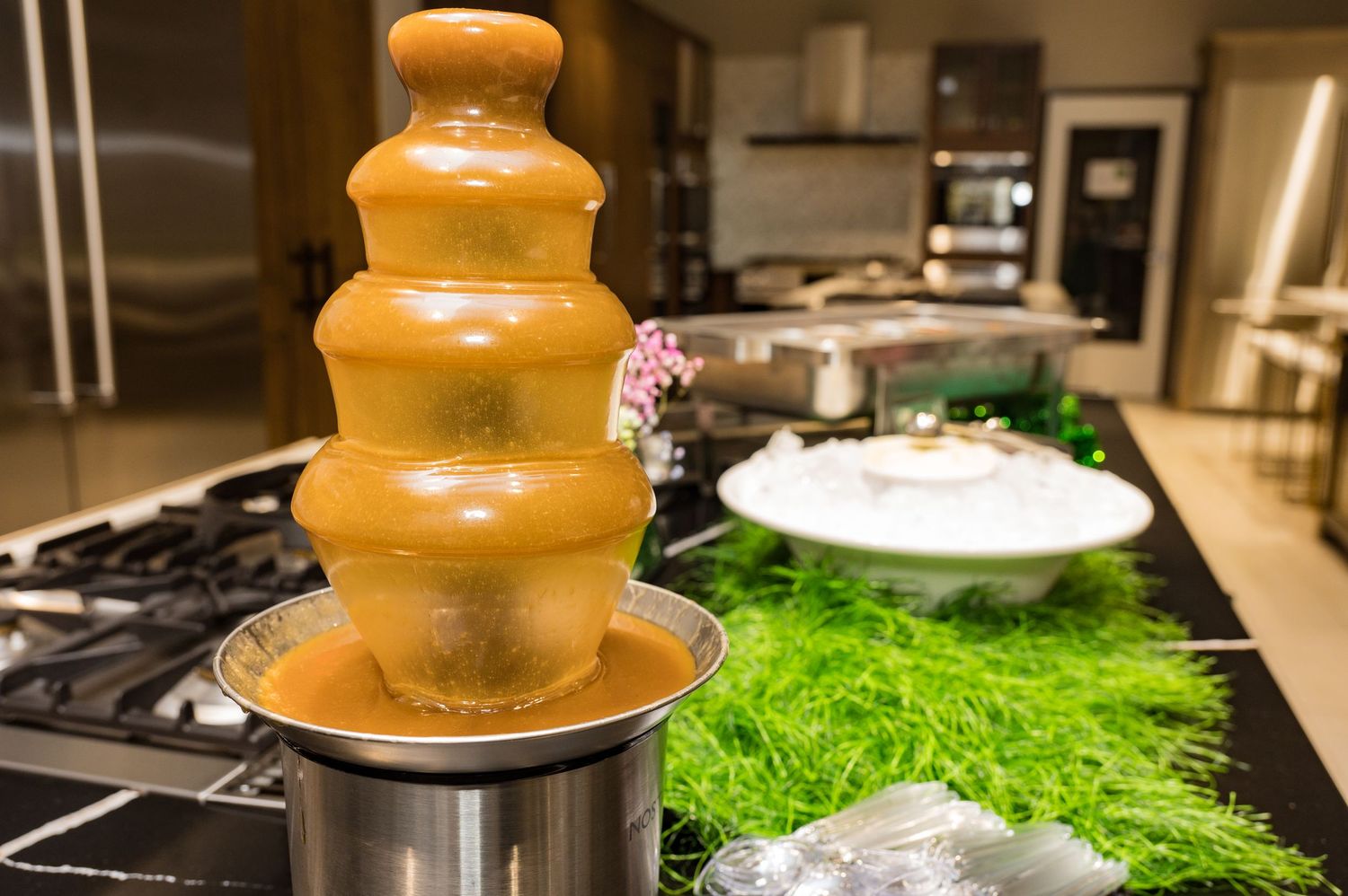 Golden caramel chocolate fountain on a stovetop with green grass decoration at a party display.