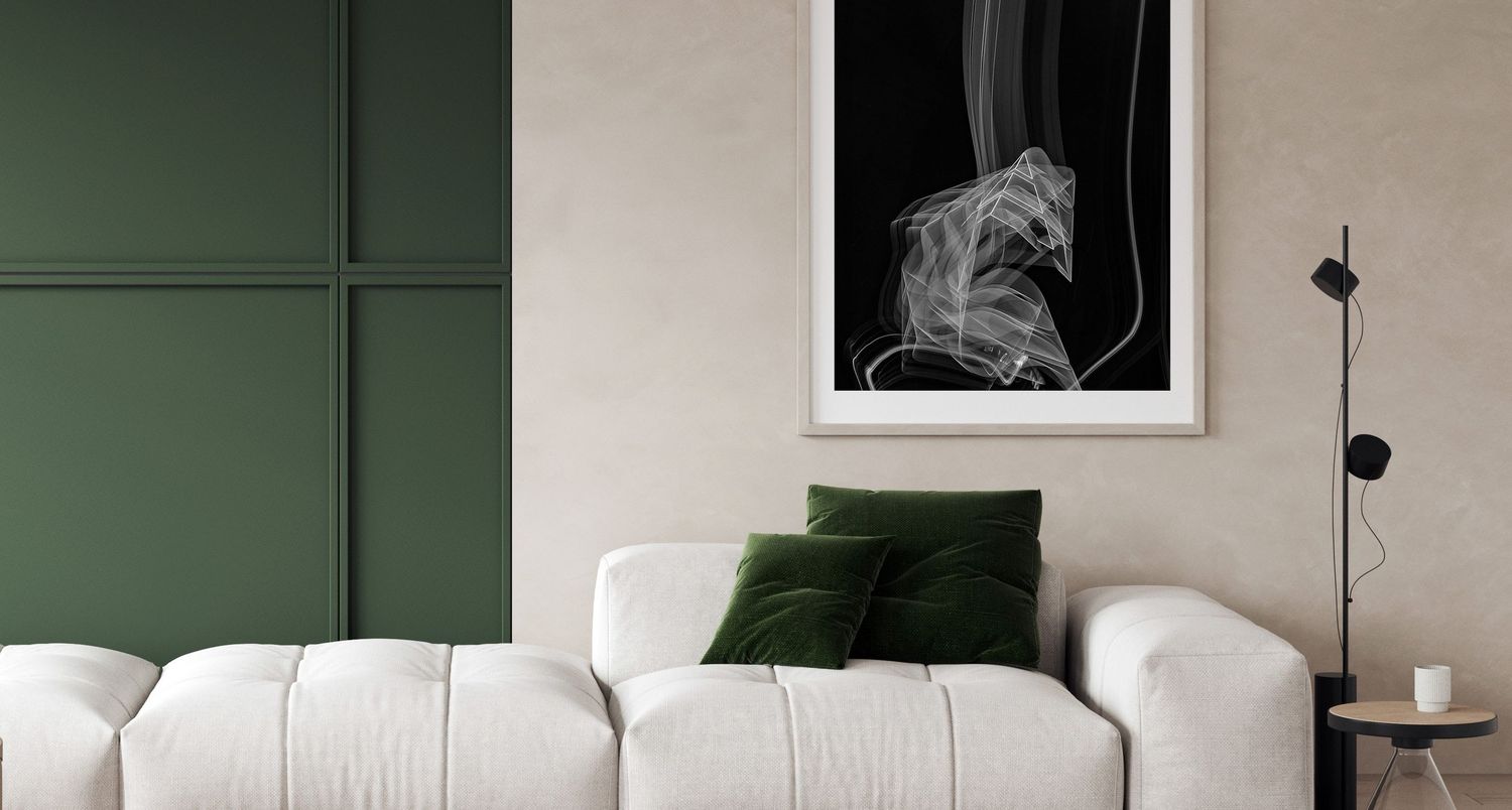 Modern living room with white sofa, green velvet pillows, and abstract black and white framed art on a sage green wall.