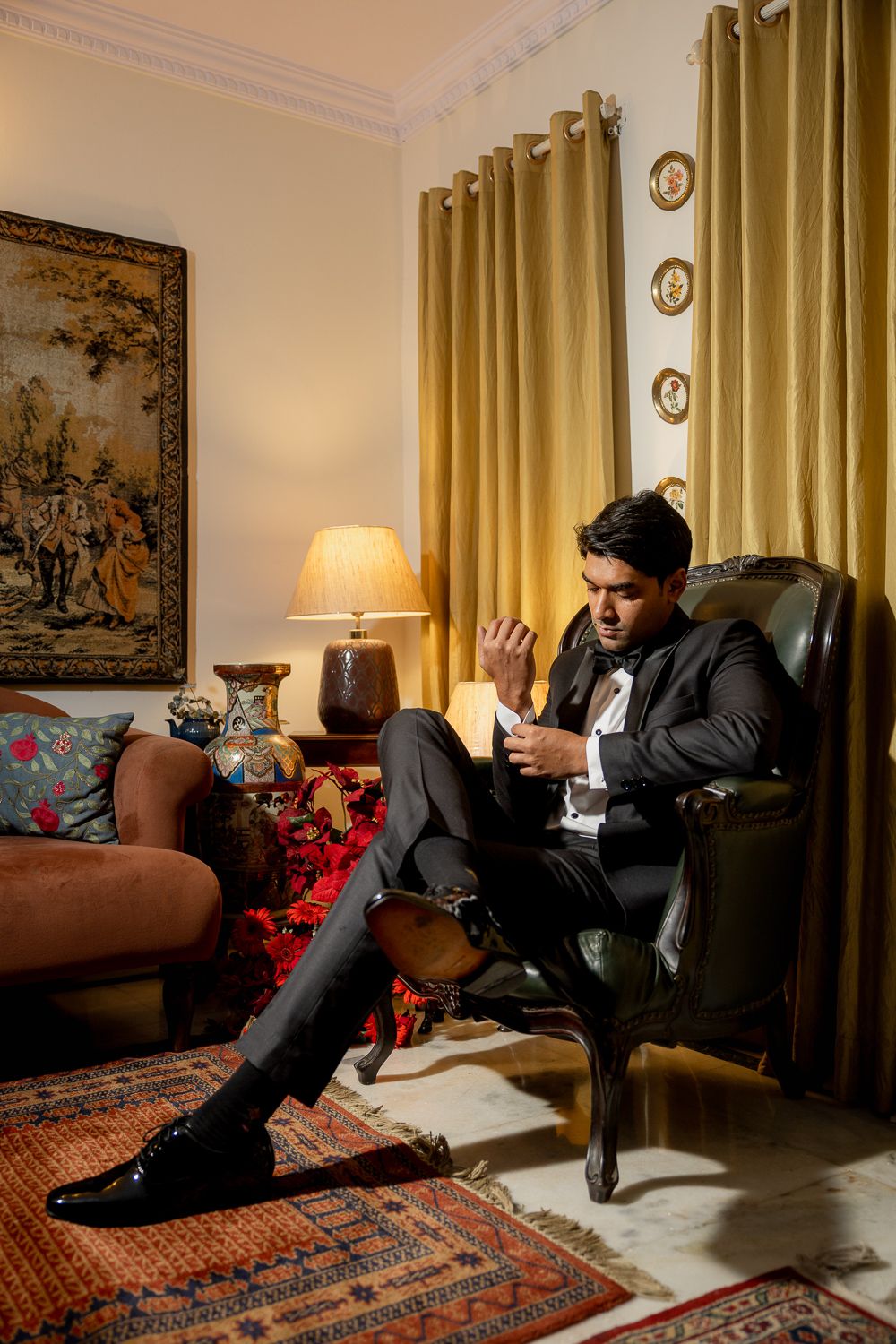 A person in a dark suit lies dramatically on a brown couch in an elegant room with gold curtains and oriental decor.