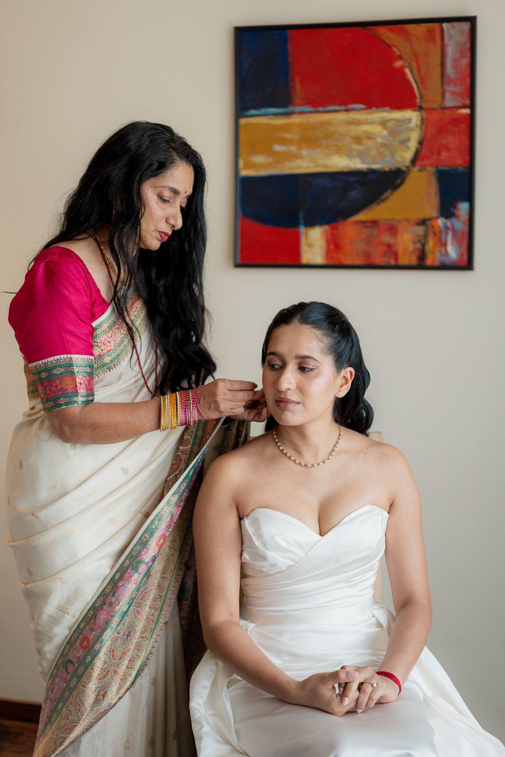 A series of five photos showing someone in a white dress being helped into a floral sari by another person.