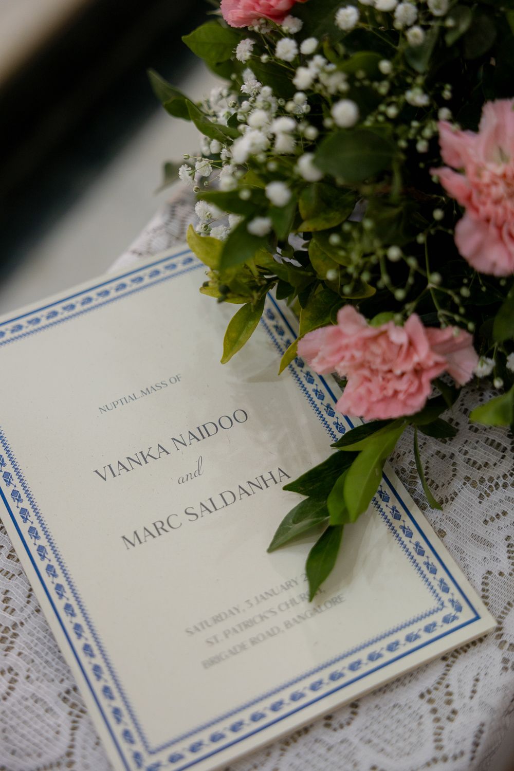 Wedding place cards with names displayed alongside delicate pink flowers and white baby's breath on lace tablecloth.