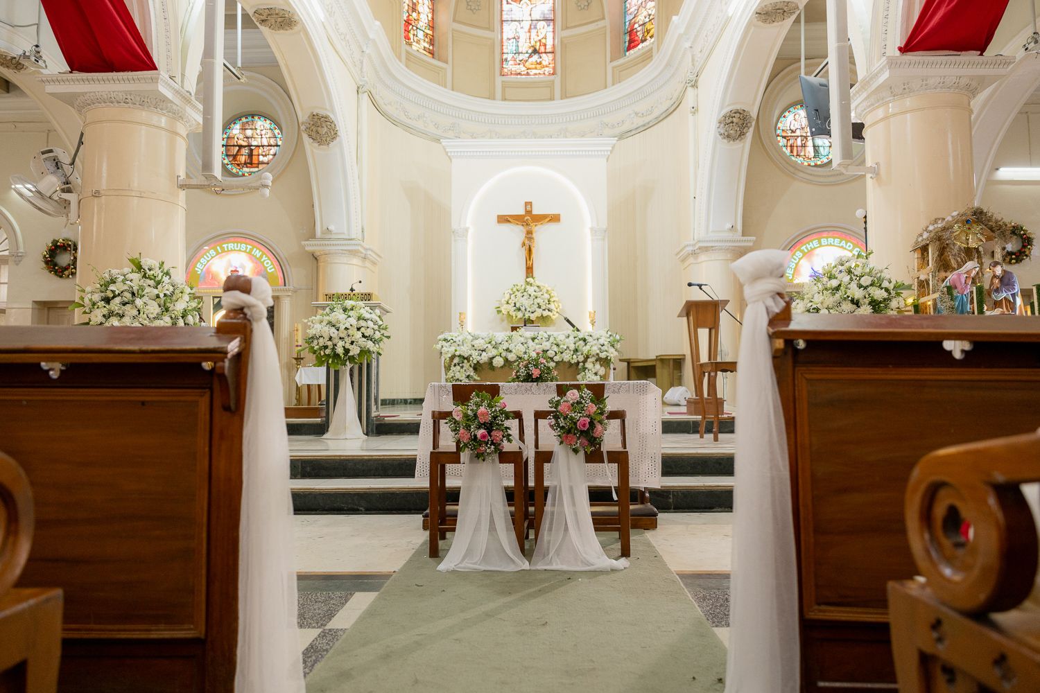 Interior view of a traditional Catholic church sanctuary with white columns, stained glass windows and floral decorations.