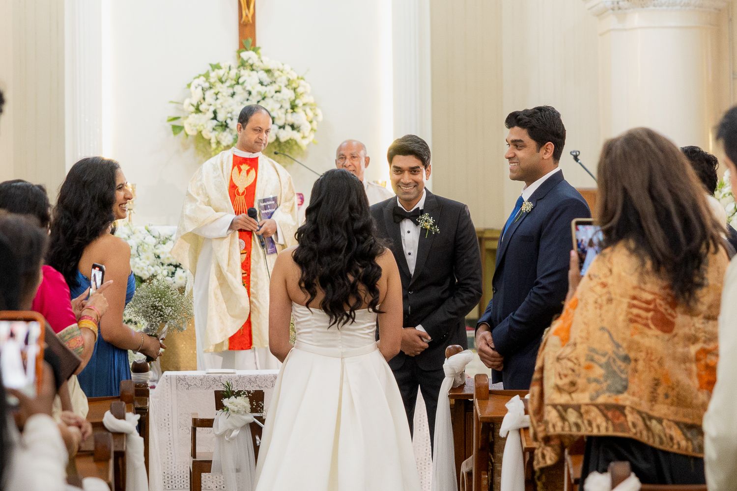 Wedding ceremony procession in a traditional church setting with guests seated in wooden pews.