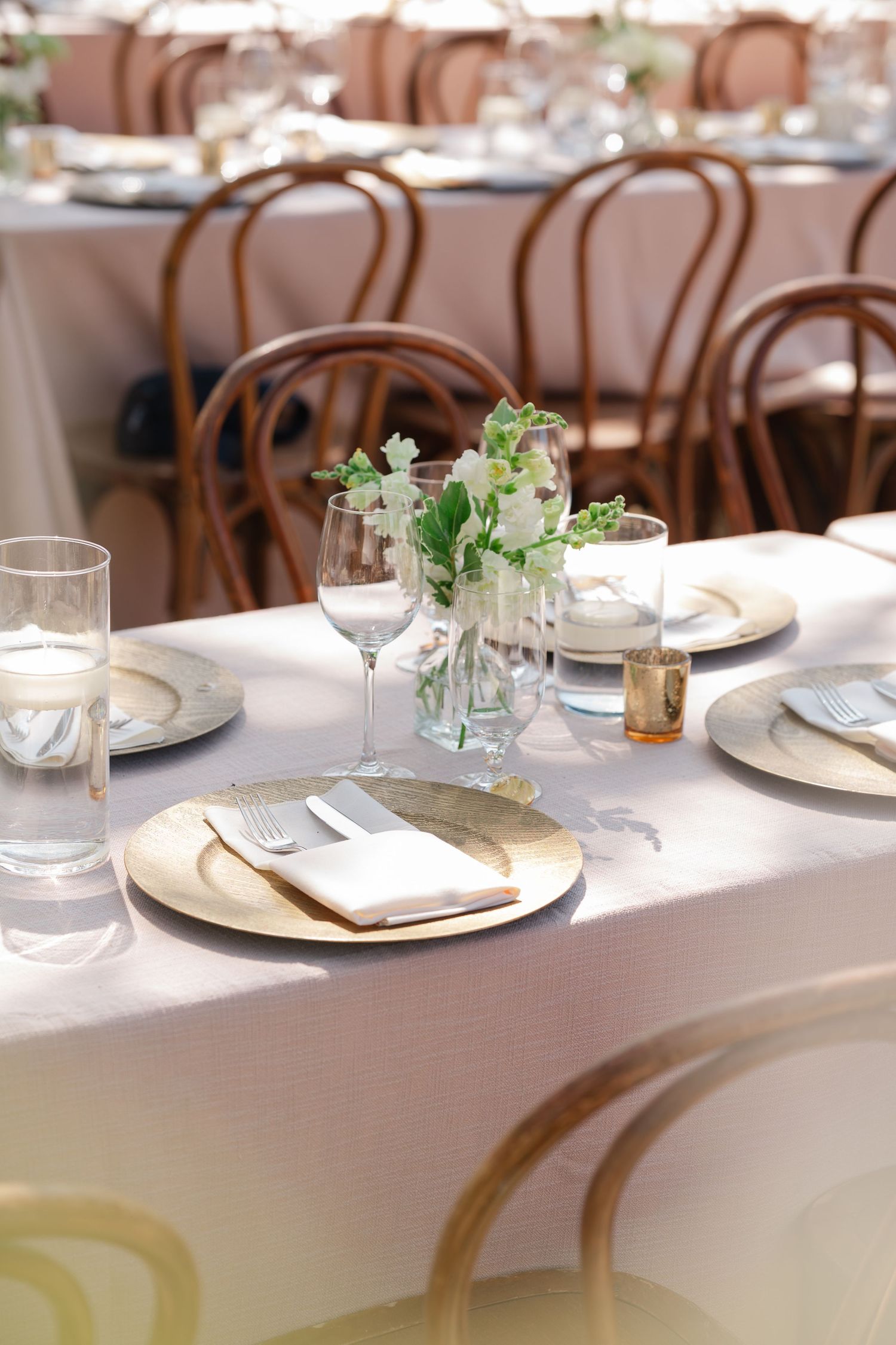 Elegant table settings with white linens, glassware and wooden chairs in a bright restaurant dining room.