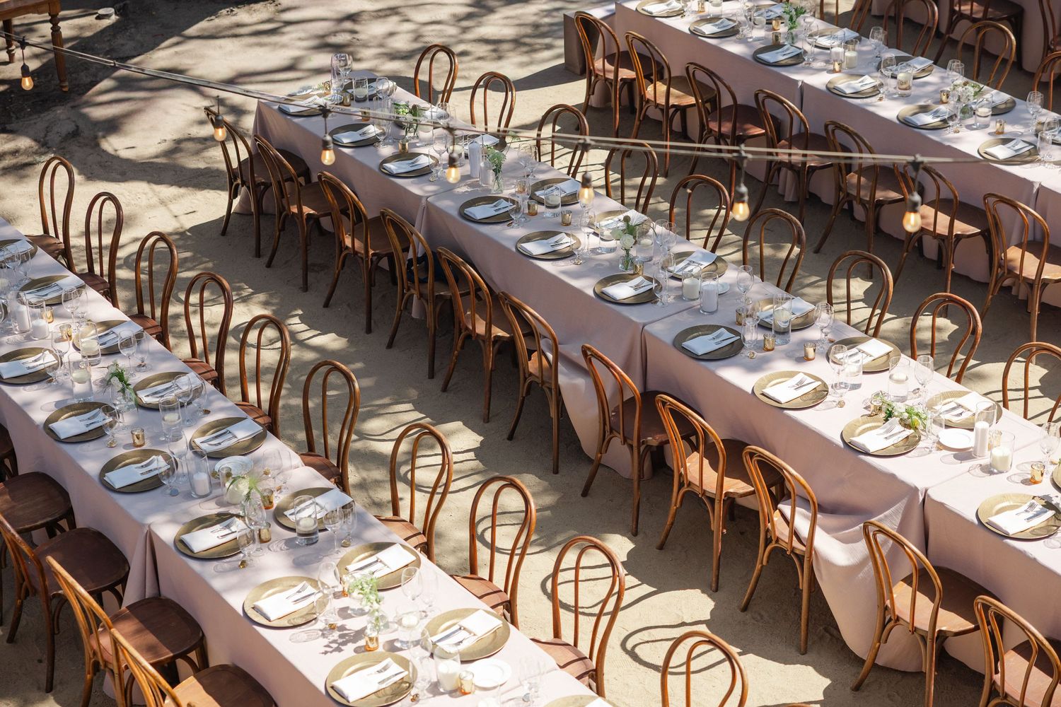 Long wooden dining tables with elegant place settings arranged in a rustic banquet hall with bentwood chairs.