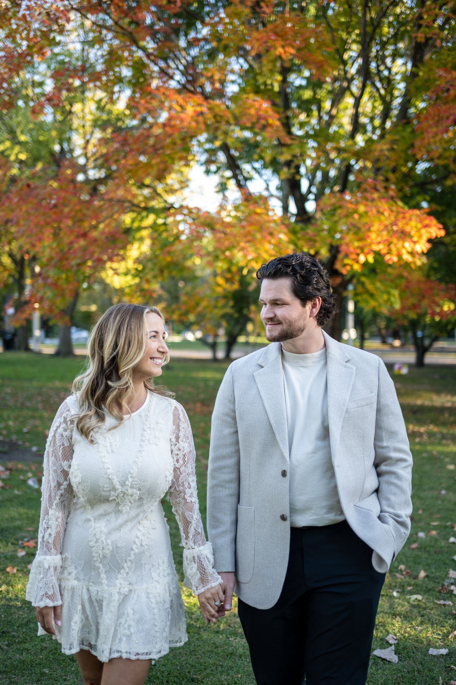 A couple walks along a paved path with the Chicago skyline visible in the background on a sunny autumn day.